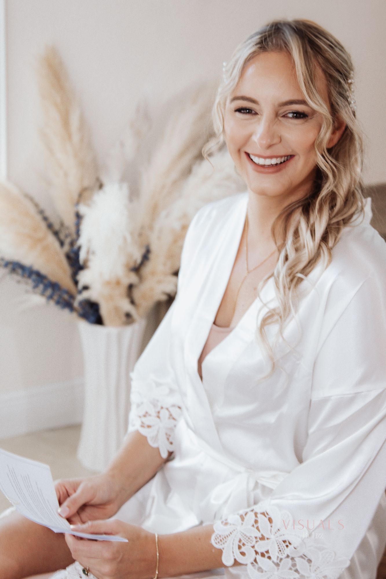 Getting ready scene with woman in white lace robe smiling during wedding preparations.