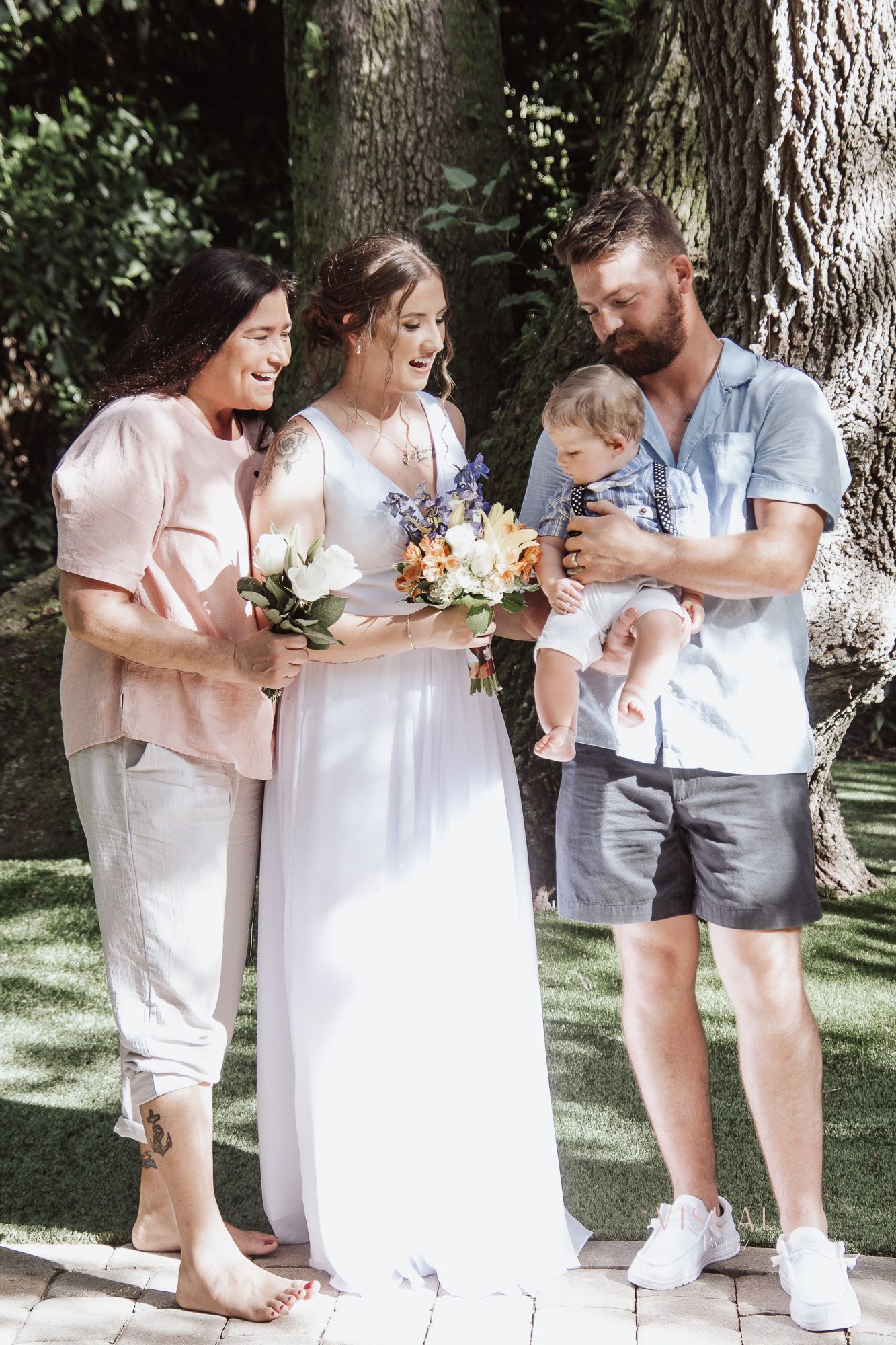 Five heartwarming candid photos show a touching family moment outdoors beneath a large tree on a wedding day.