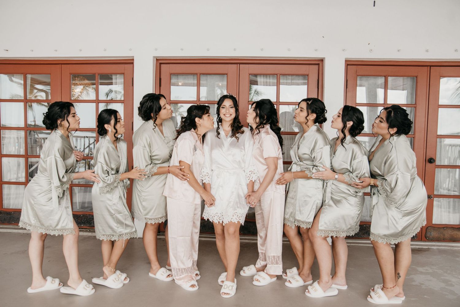 Wedding party members in matching white robes sit in line on floor during preparation.