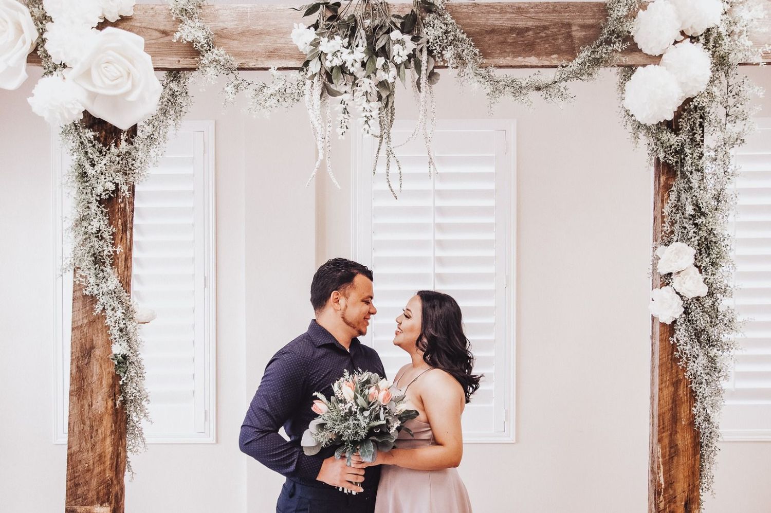 Romantic wedding couple shares tender moments in a light-filled venue decorated with elegant white floral arrangements.