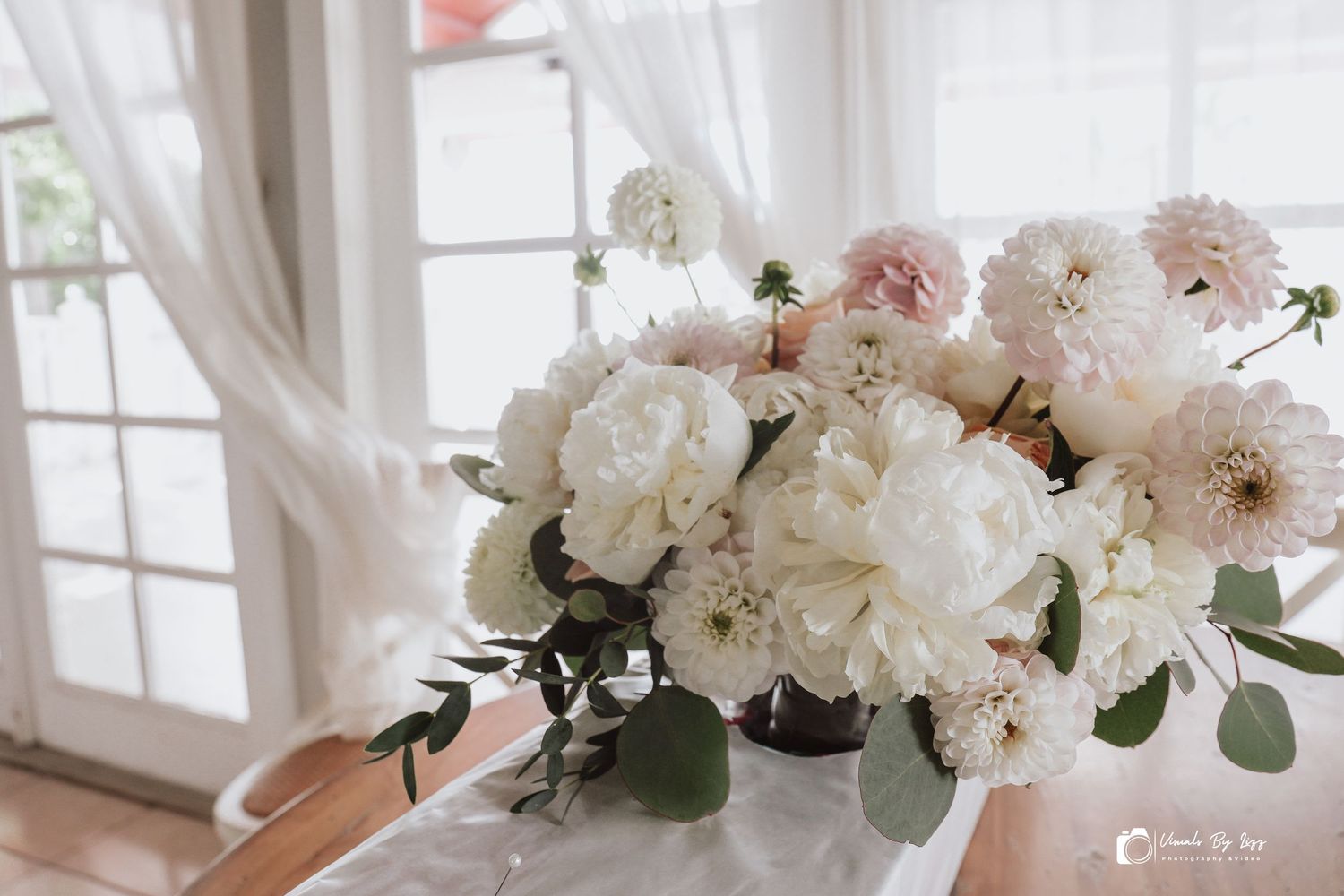 White and blush pink peonies arranged in elegant glass vases create a romantic wedding reception centerpiece display.