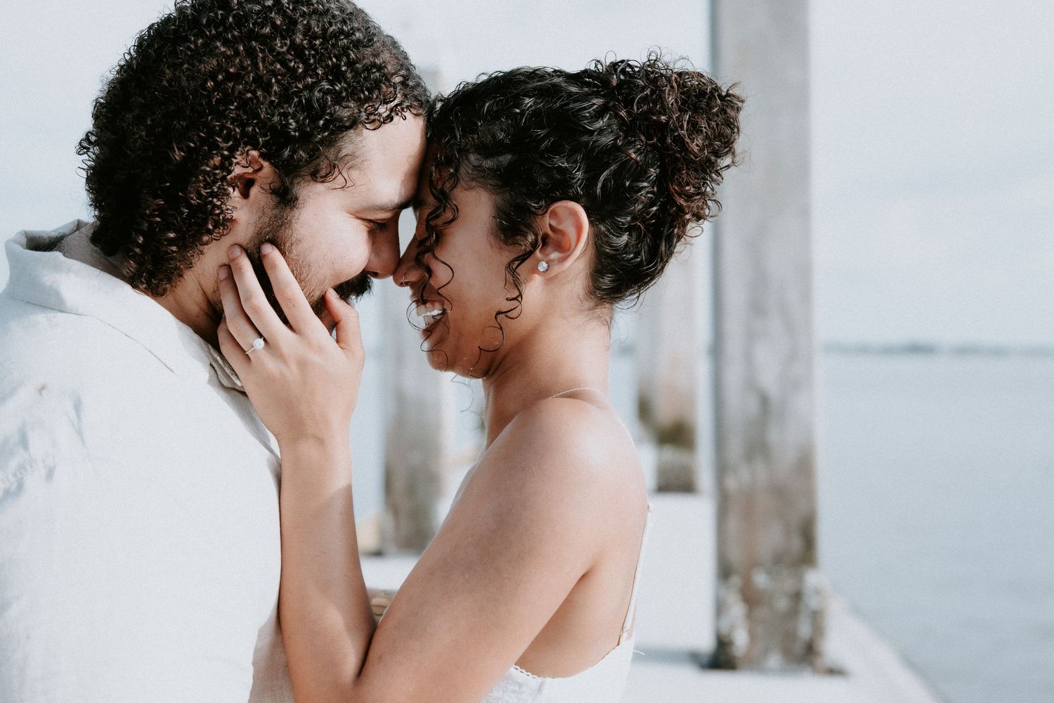 Romantic couple sharing an intimate moment outdoors near water, touching foreheads and smiling on a sunny day in Jacksonville, Florida.