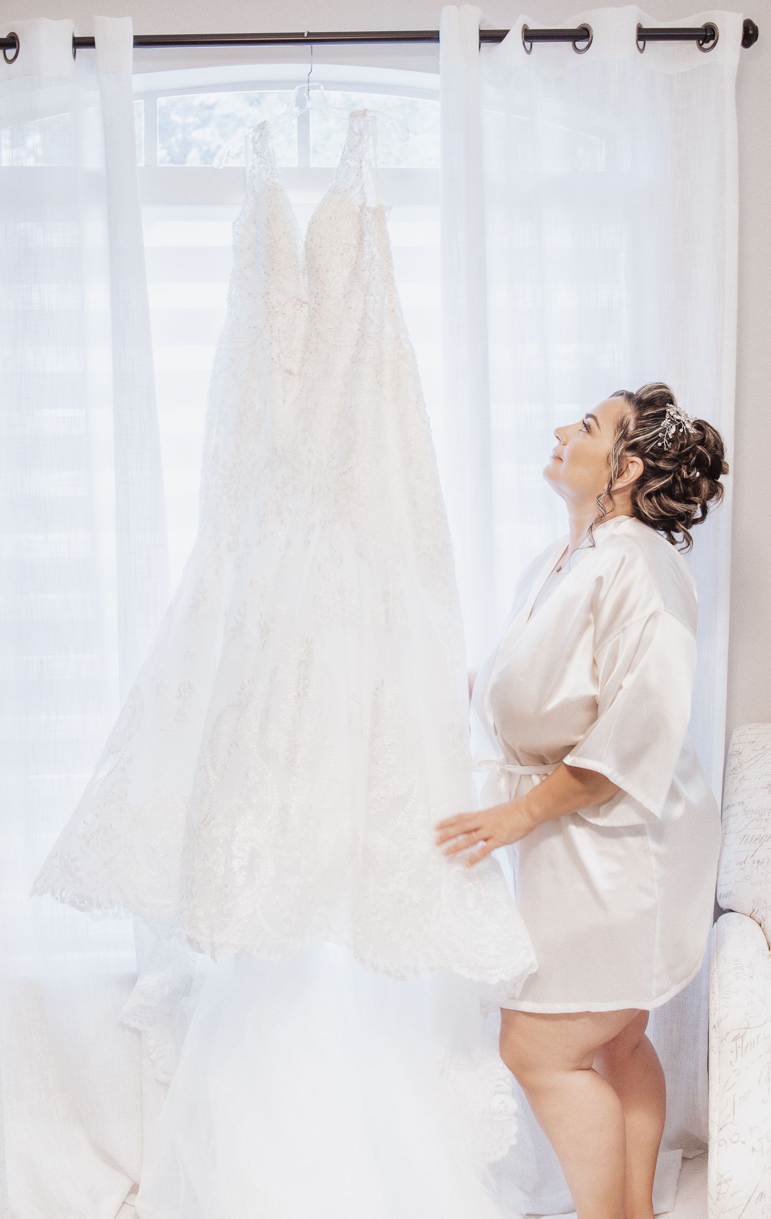 Bride in white robe playfully posing with wedding dresses in background.