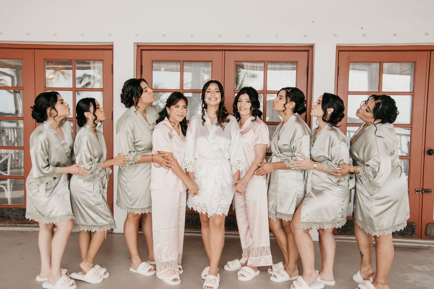 A group of women wearing matching satin robes pose together in a hallway before a special event.