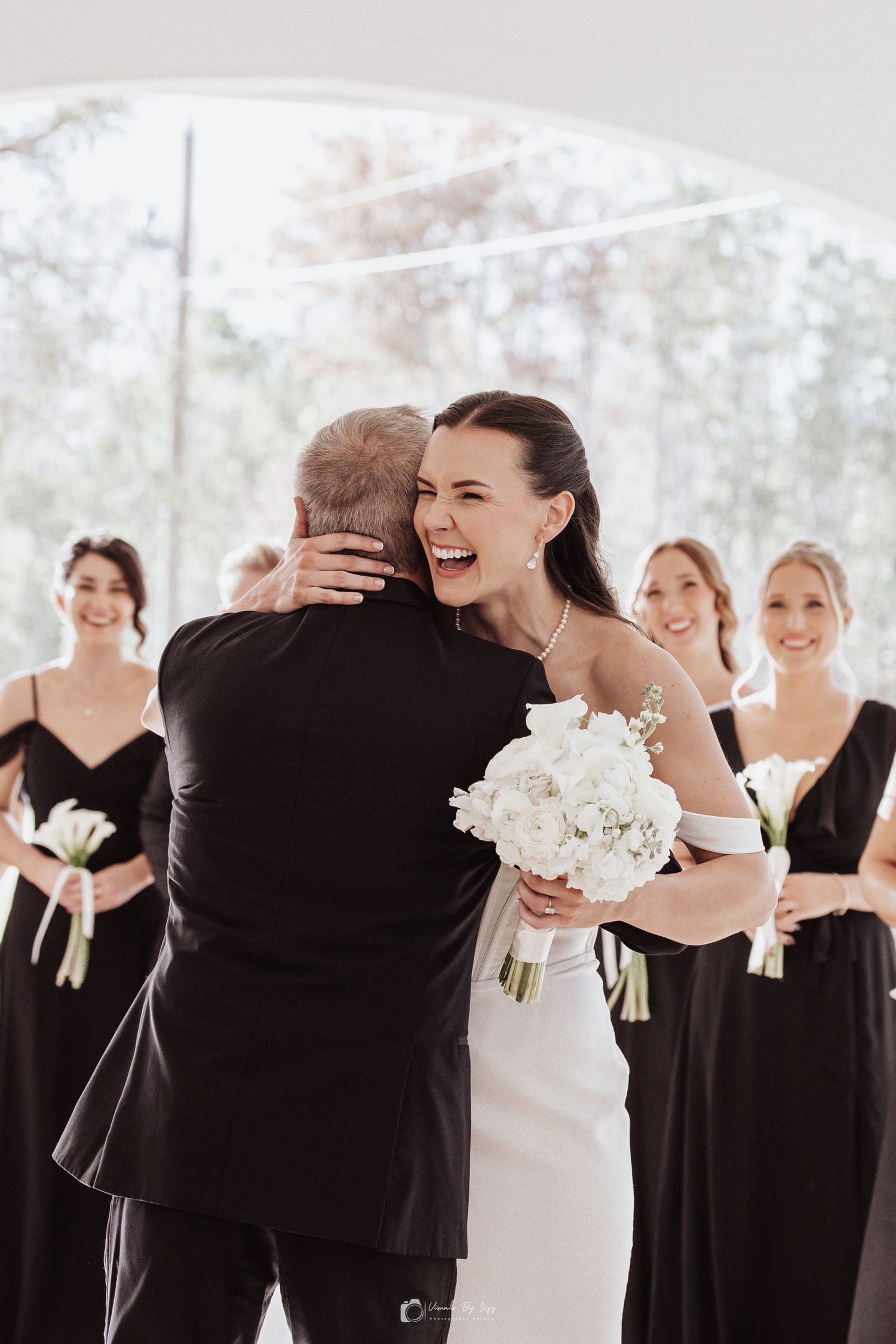 A wedding party in black dresses and a white gown share joyful laughter and embraces during formal photos. De Leon Springs, Fl