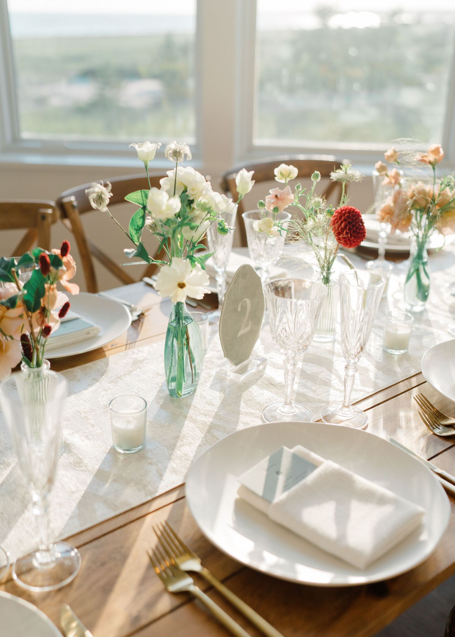 Elegant wedding table setting with floral bud vases, crystal glassware, white plates, gold cutlery, and a table number card. Wychmere