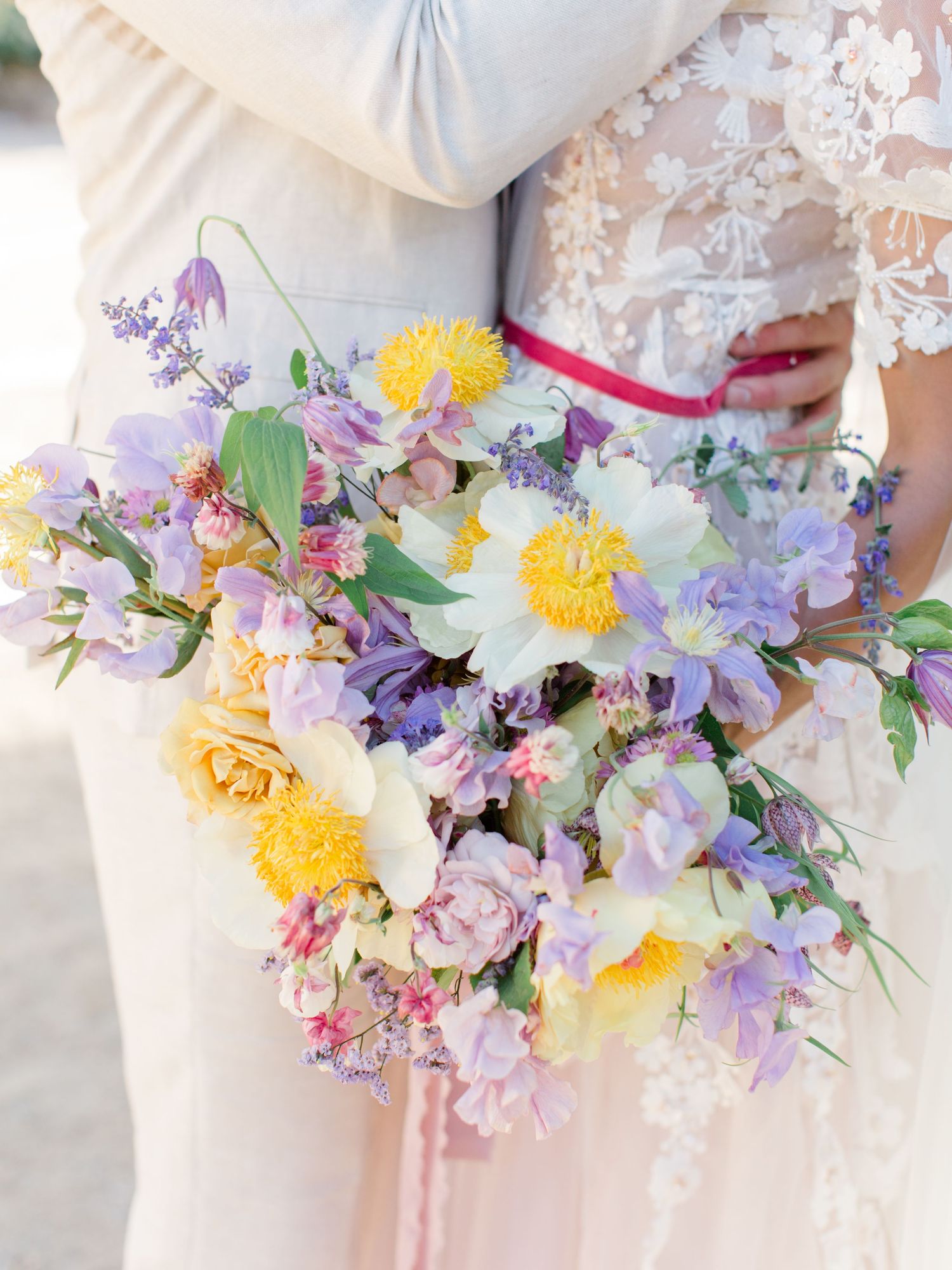 A bride holds a vibrant wildflower bouquet featuring purple, yellow, and white blooms with lush greenery. Allegretto Vineyards, Paso Robles