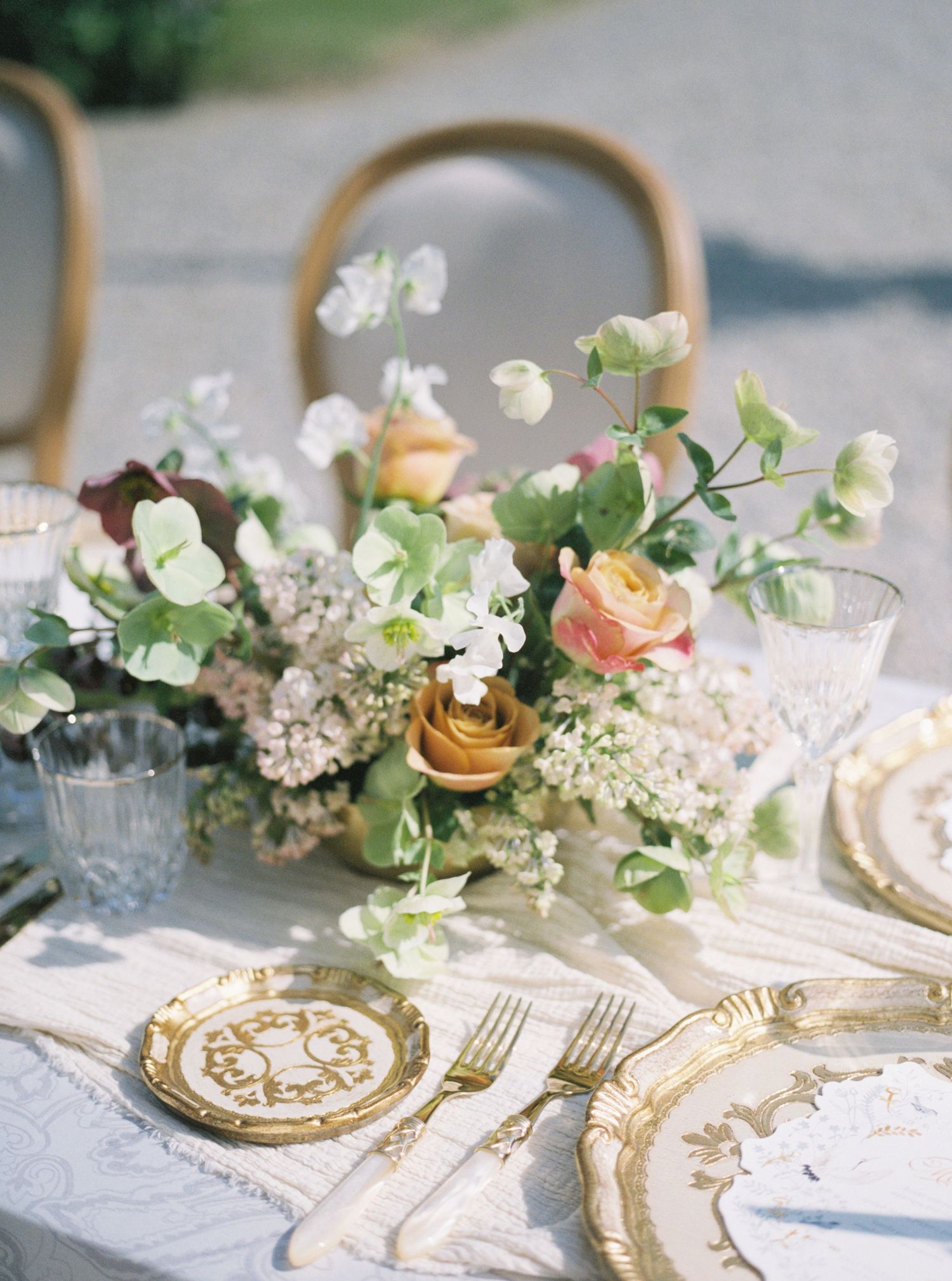 Elegant wedding table in Lake Como, Italy with gold-trimmed china, crystal glasses & a floral centerpiece of peach roses and white blooms.