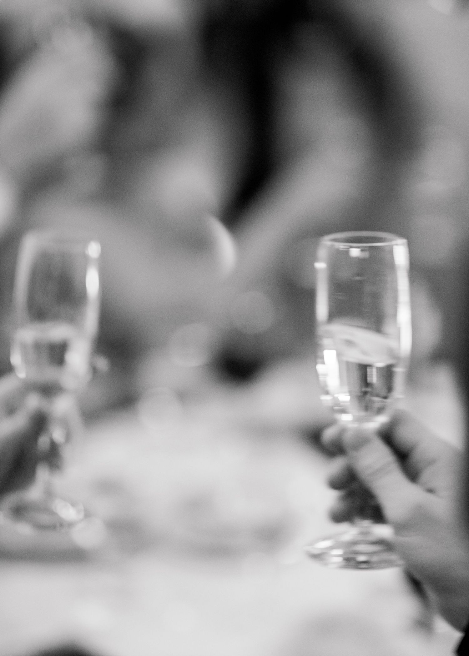 Black and white photo of hands holding champagne flutes at an elegant dinner party toast celebration.