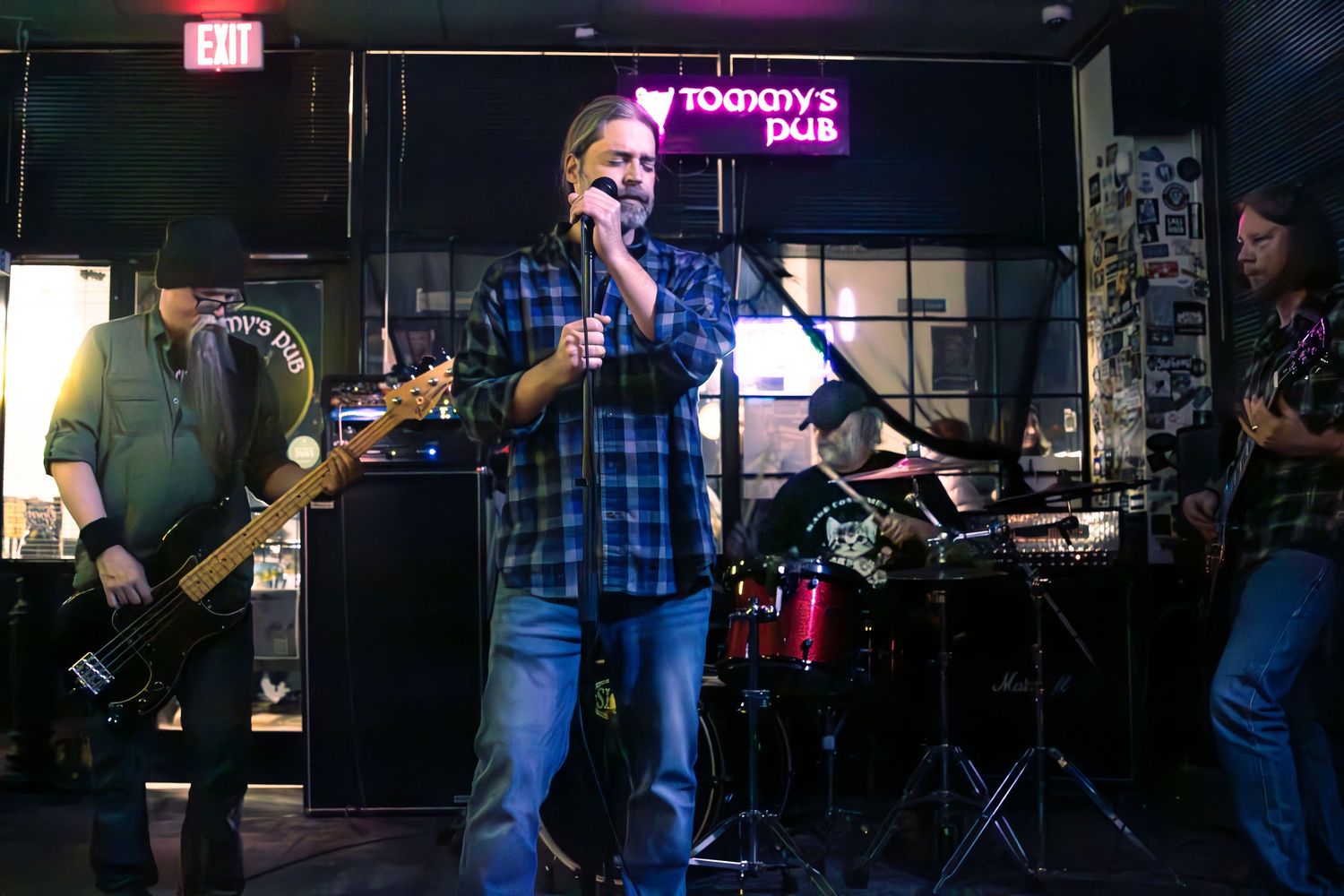 Rock band performing live at Tommys Pub with vocalist singing into microphone on stage.