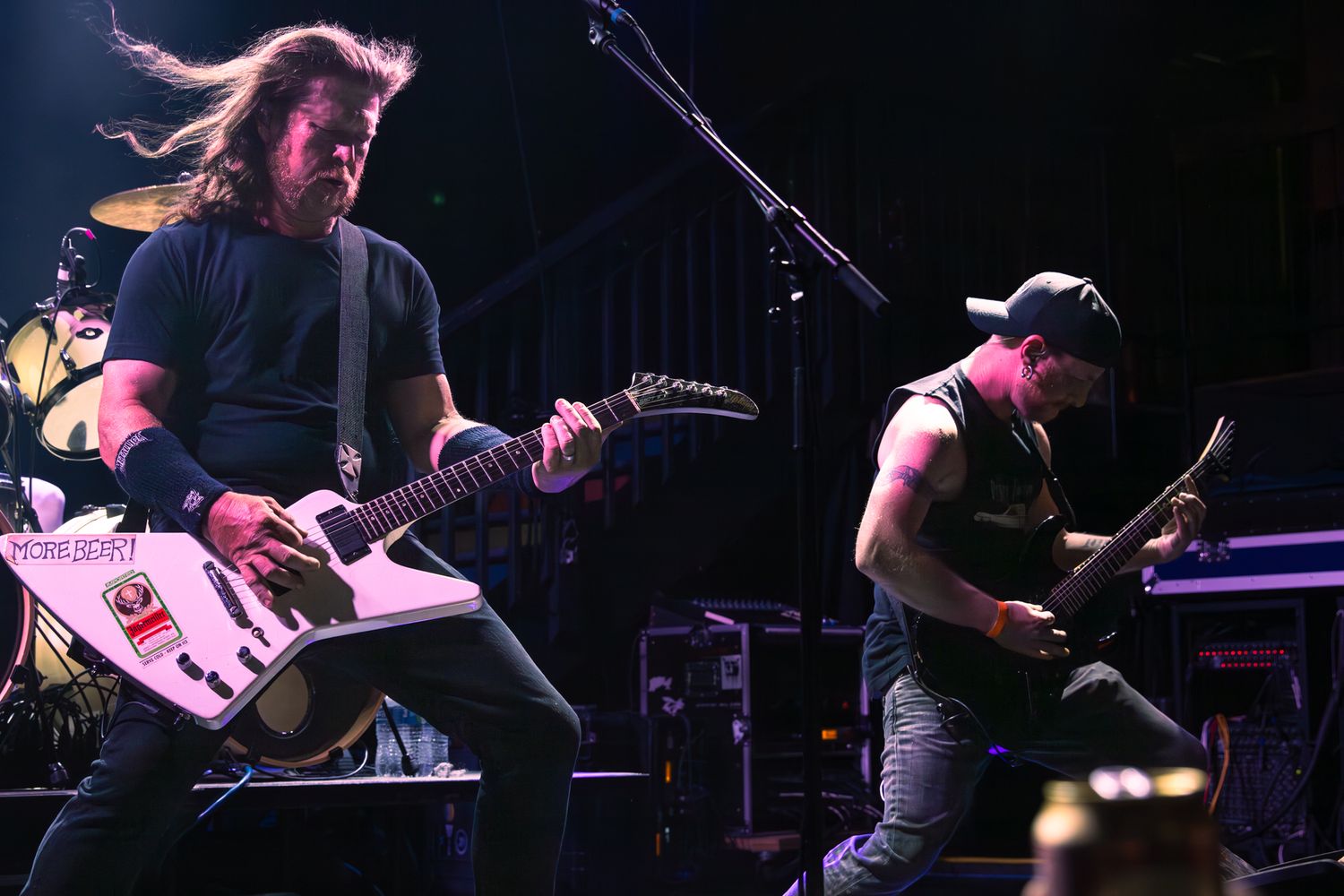 Two guitarists performing on stage at a live rock concert under bright stage lights.