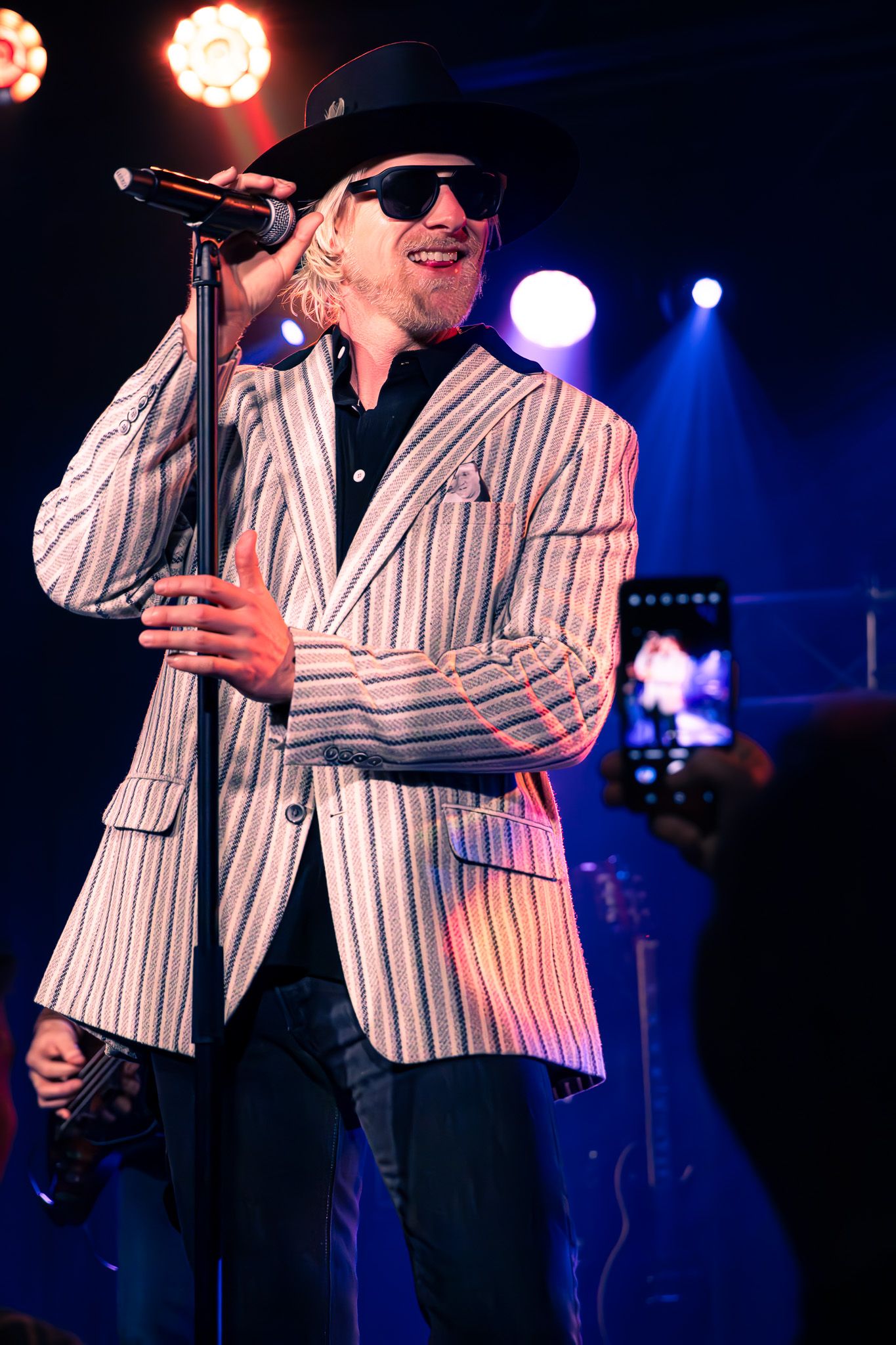 Male vocalist in striped blazer and black hat performing on stage under warm concert spotlights in Charlotte, NC.