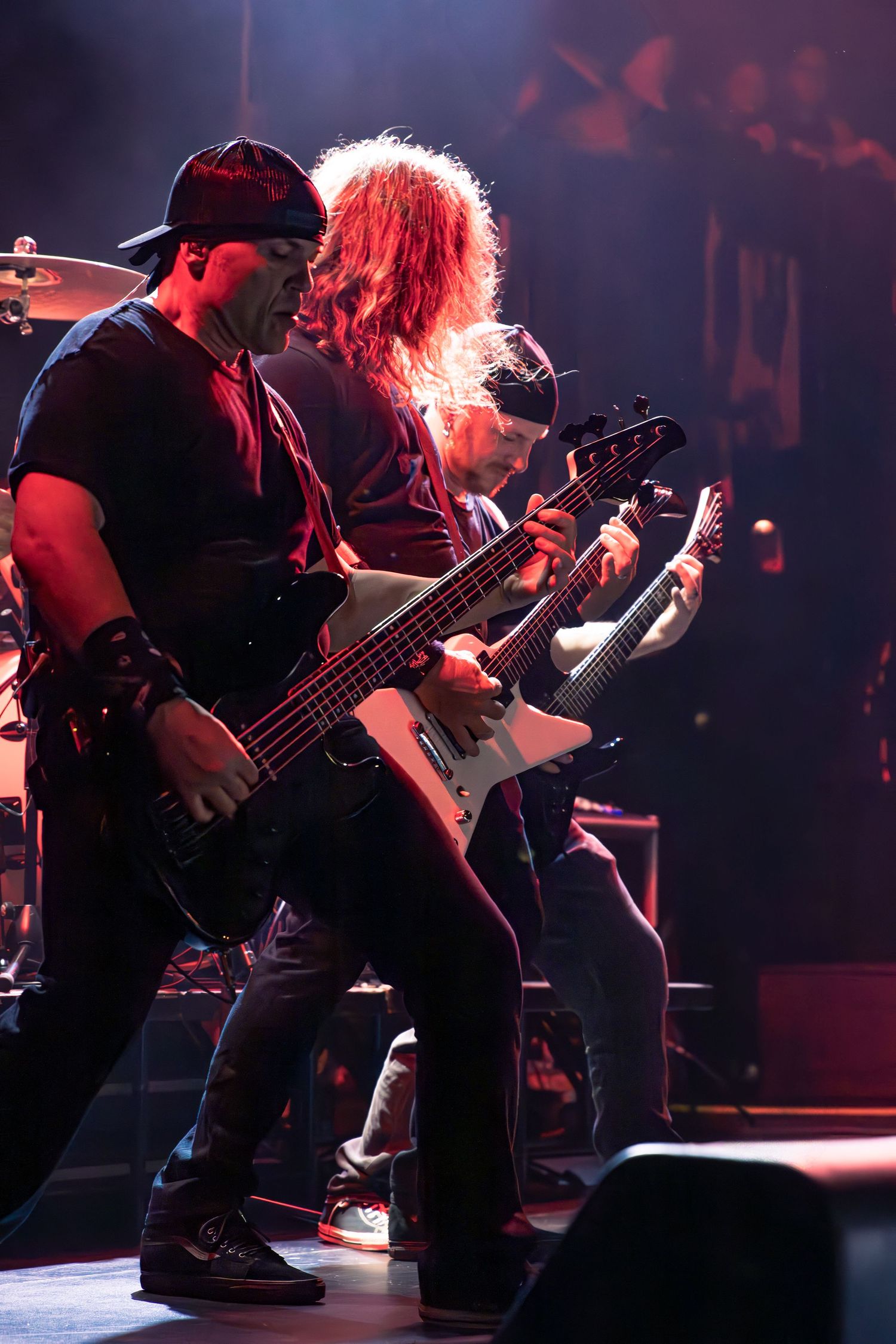 Heavy metal guitarists playing electric guitars on stage under dramatic red concert lighting.