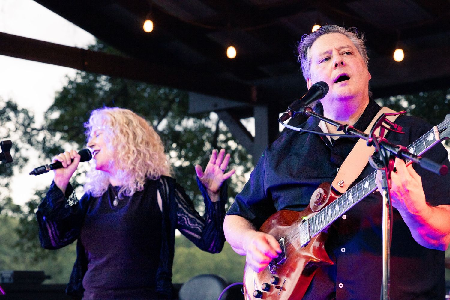 A female vocalist and male guitarist performing live on an outdoor stage at night in Monroe, NC.