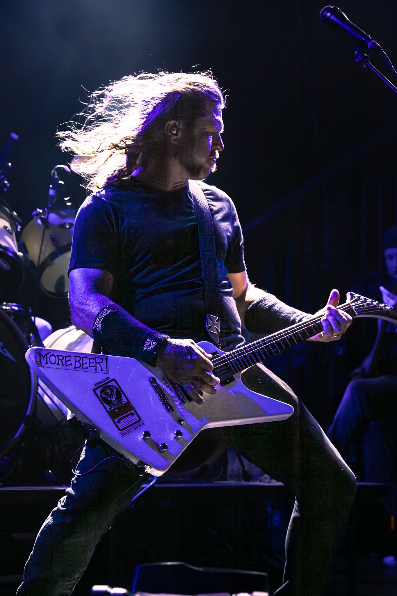 Long-haired rock guitarist performing on stage with a white Flying V electric guitar under blue stage lighting.