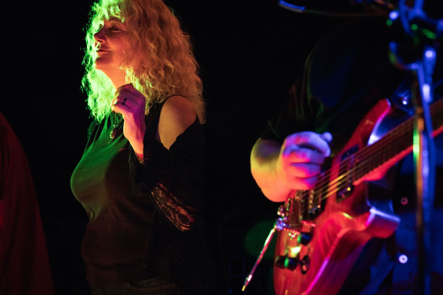 Female singer performing on stage under colorful green and red lights with a guitarist beside her.