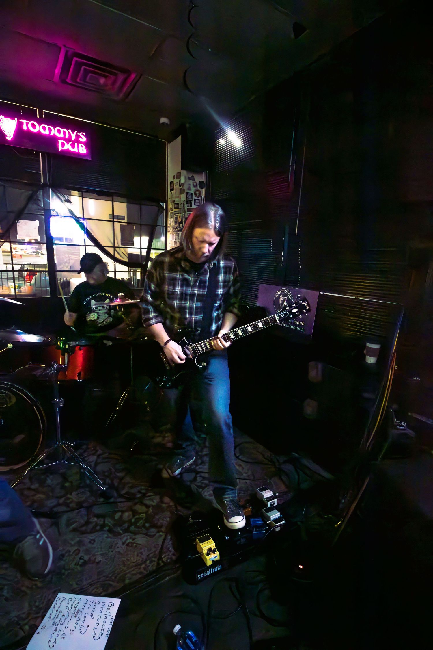 Guitarist in plaid shirt playing electric guitar on stage at Tommys Pub venue.