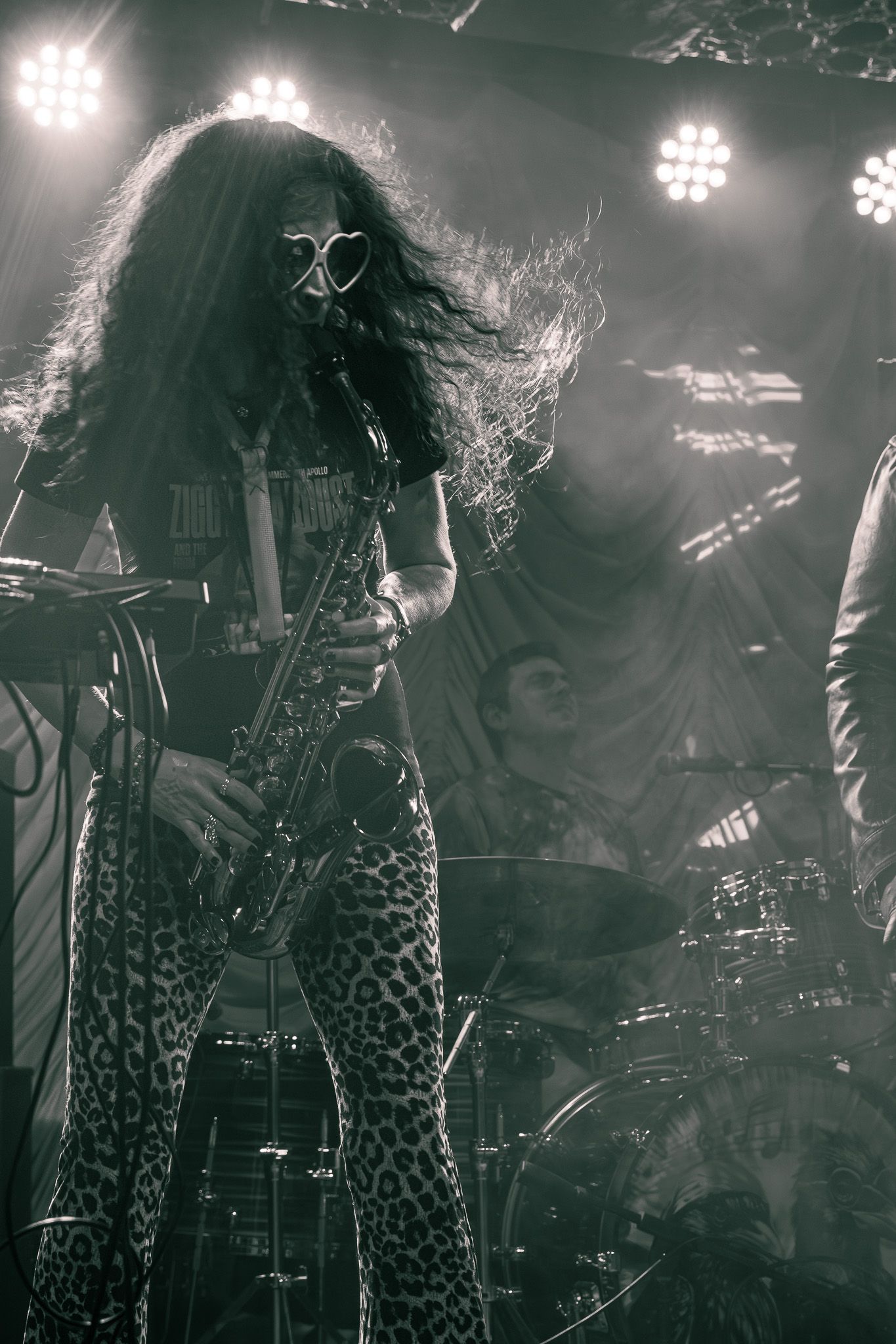 Black and white photo of wild-haired guitarist in leopard pants shredding on stage.