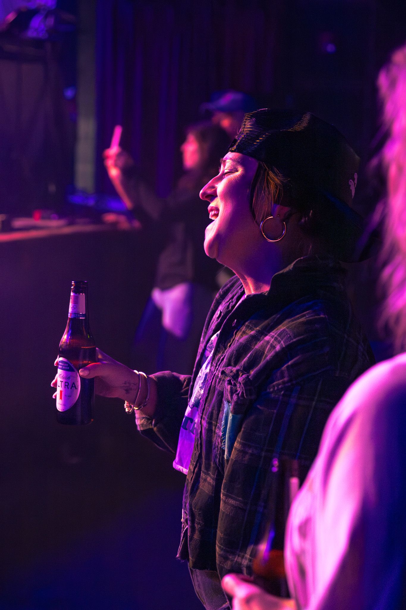 Woman holding beer bottle enjoys live concert under purple neon lights.