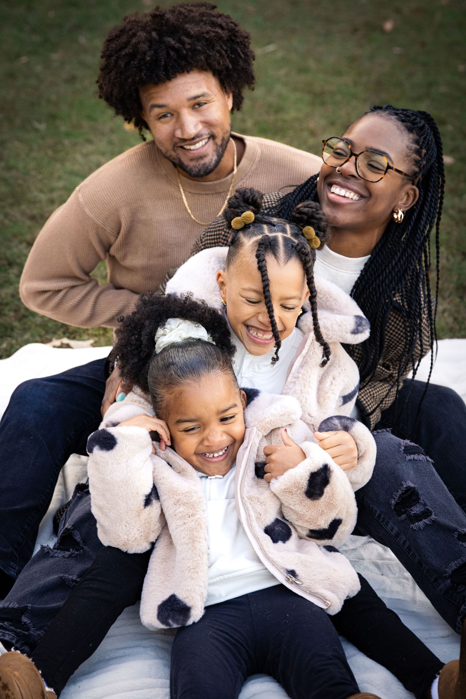 Happy African American family of five smiling and laughing together outdoors on a blanket in a park.
