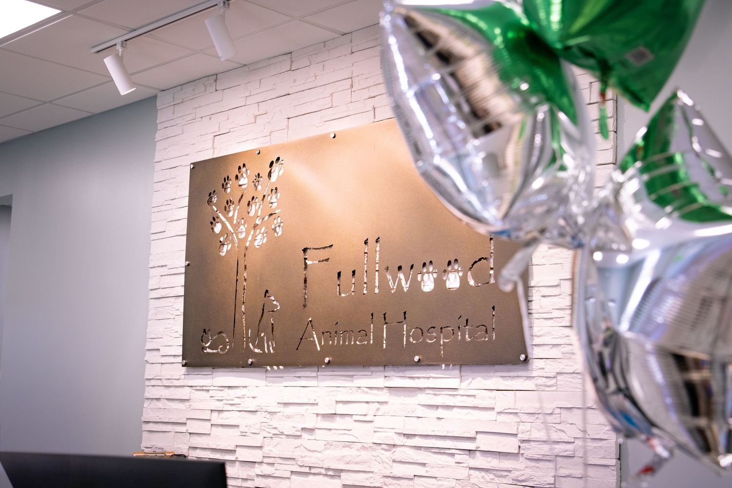 Fullwood Animal Hospital lobby sign on white stone wall with green and silver balloons.