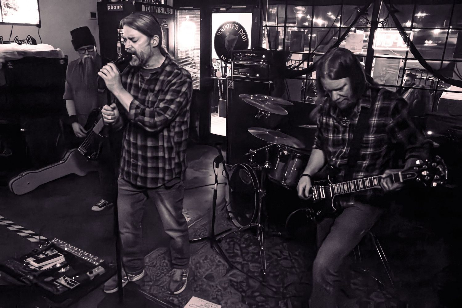 Black and white photo of a rock band rehearsing with vocalist and guitarist in plaid shirts.