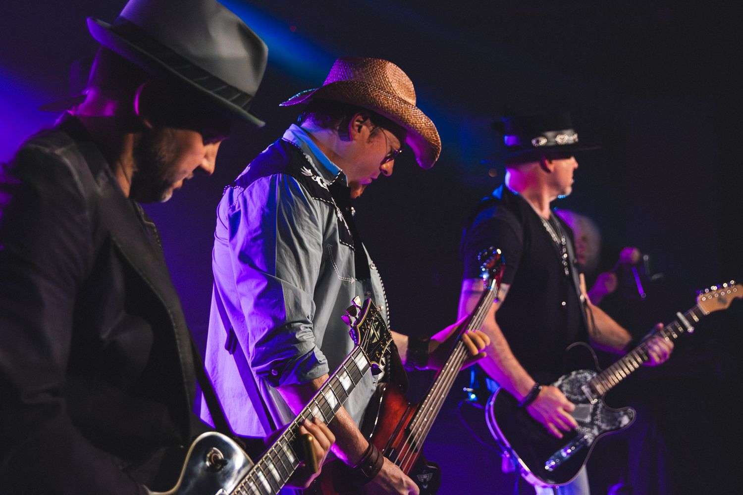 Three guitarists in cowboy hats performing together on stage under purple concert lighting in Charlotte, NC.
