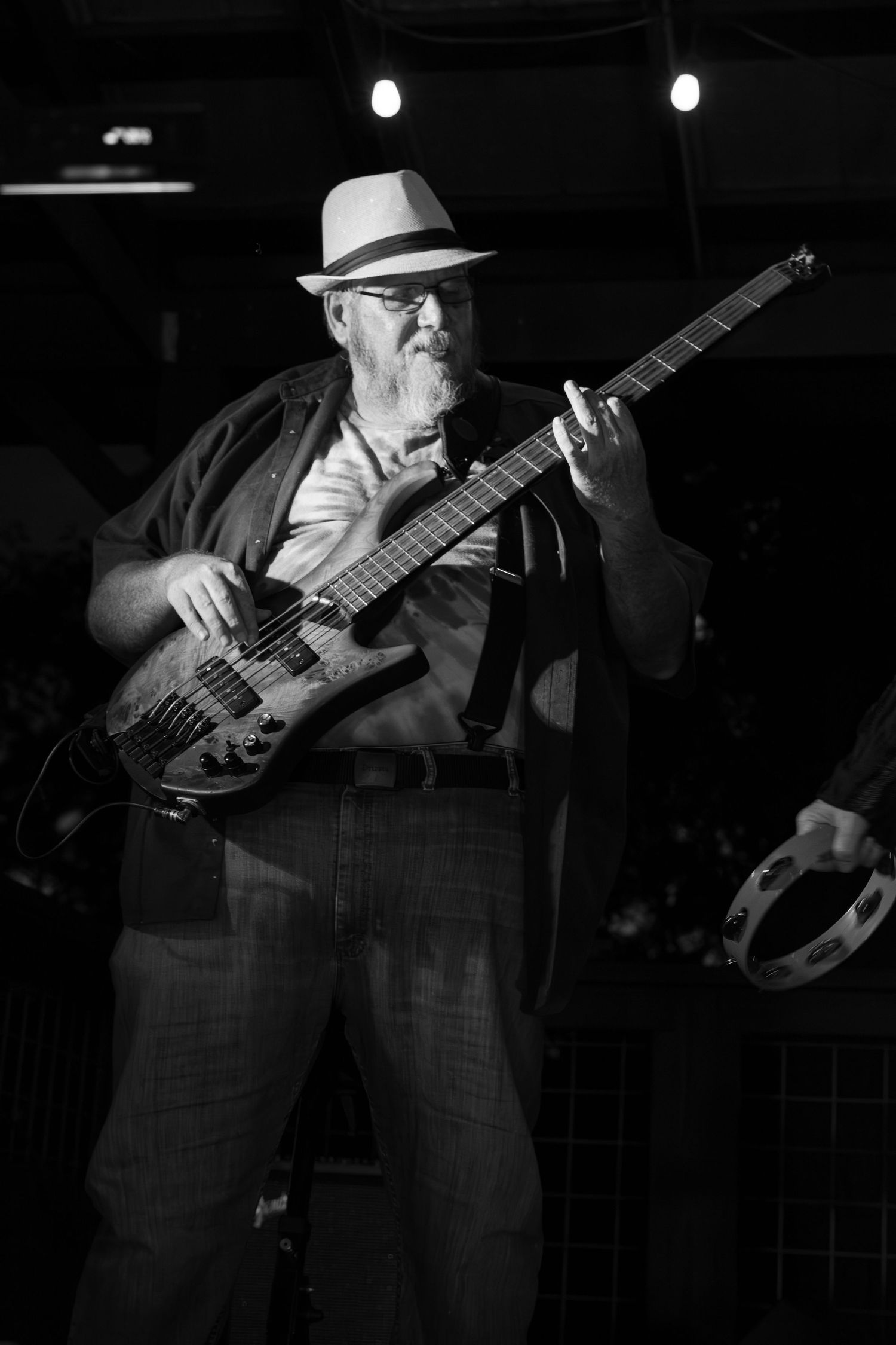 A bearded man in a fedora playing bass guitar on stage in black and white in Monroe, NC.