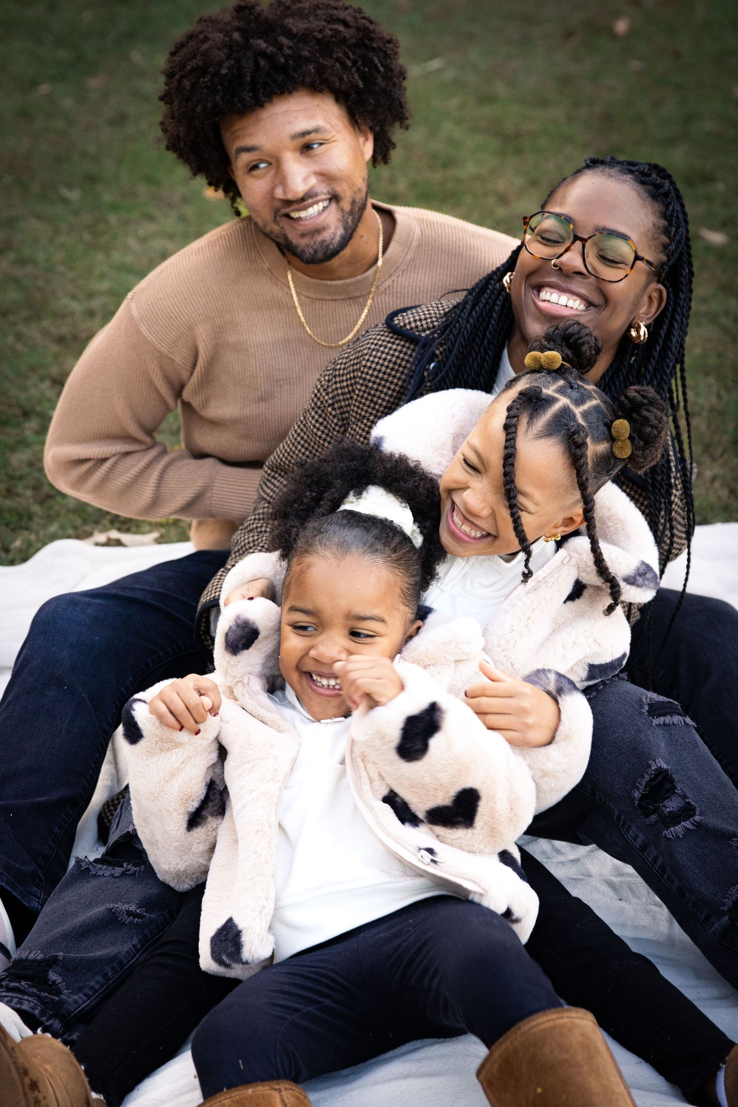 Happy African American family portrait of four laughing and cuddling together on blanket at purser Halsey park in Matthews, NC