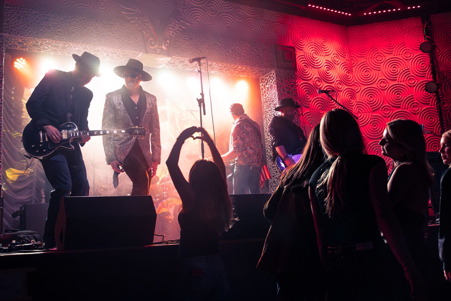 Band performing on stage with red lighting as silhouetted crowd dances below in Charlotte, NC.