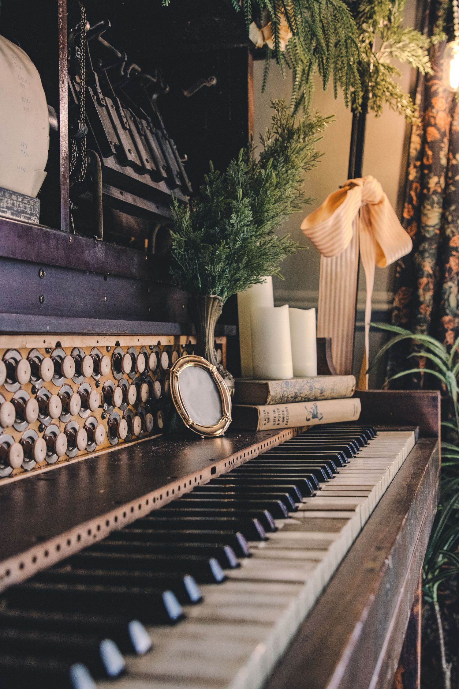 Vintage upright piano decorated with candles, books, greenery, and a peach bow ribbon.