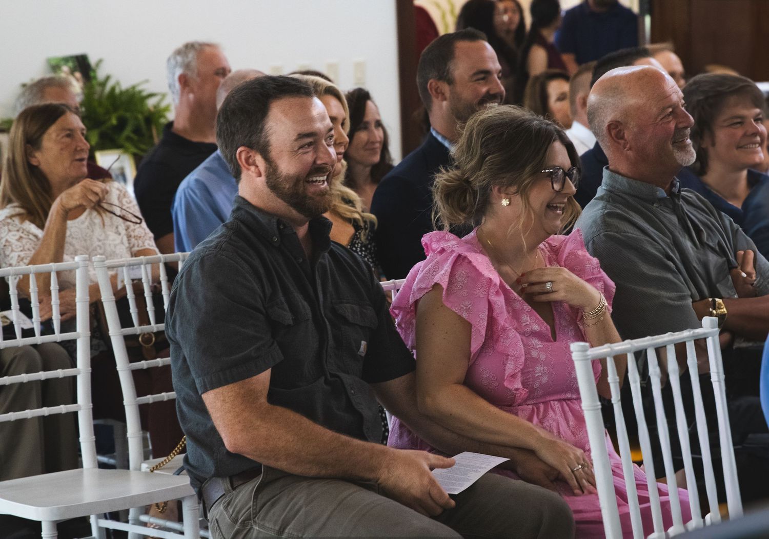 Smiling guests seated in white chairs enjoy an indoor celebration of life event in Charlotte NC.