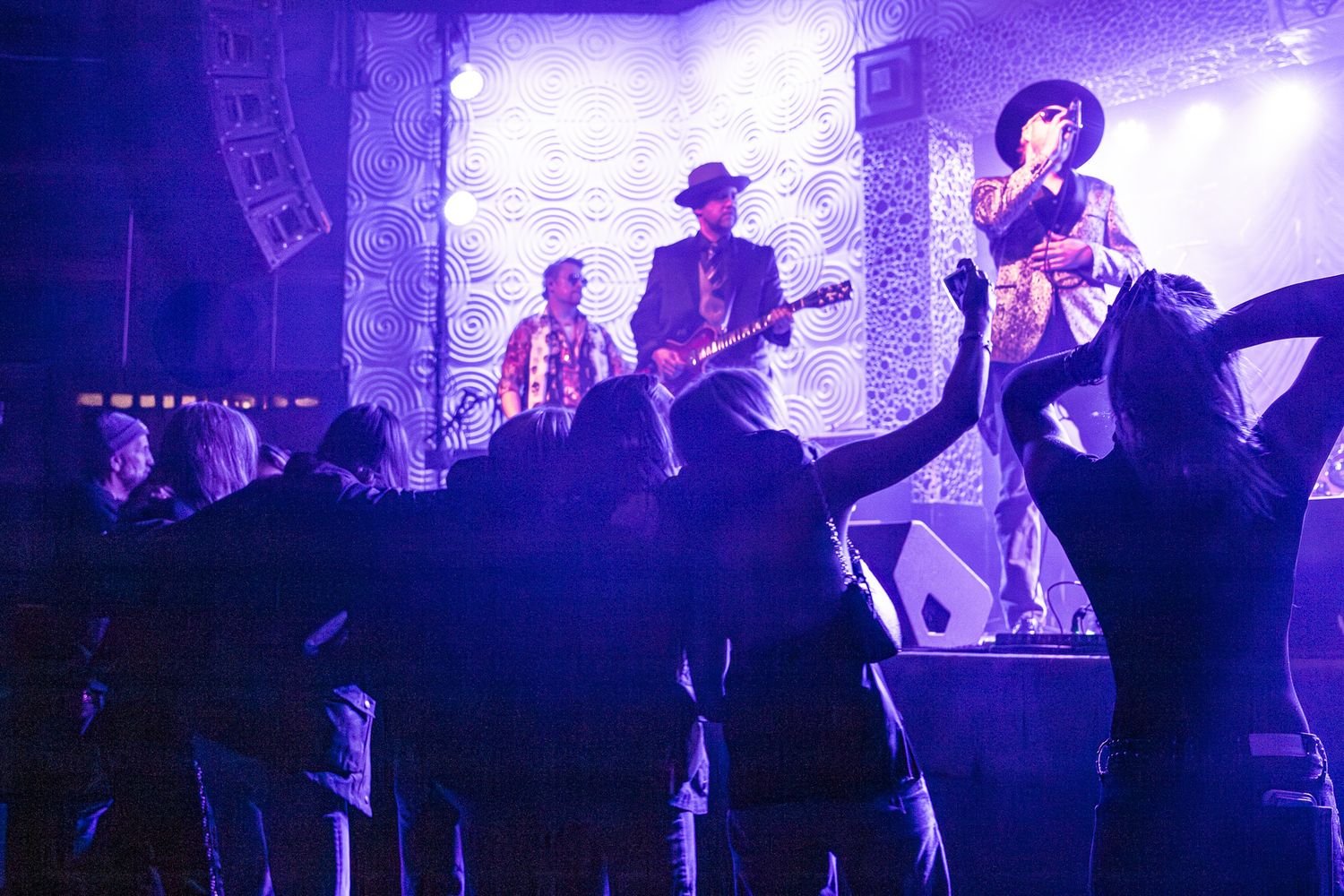 Live band performs on purple-lit stage while energetic crowd dances in foreground in Charlotte, NC.
