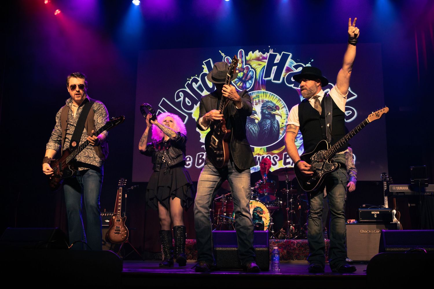 Rock band performing energetically on stage at Hard Rock venue with colorful lighting.