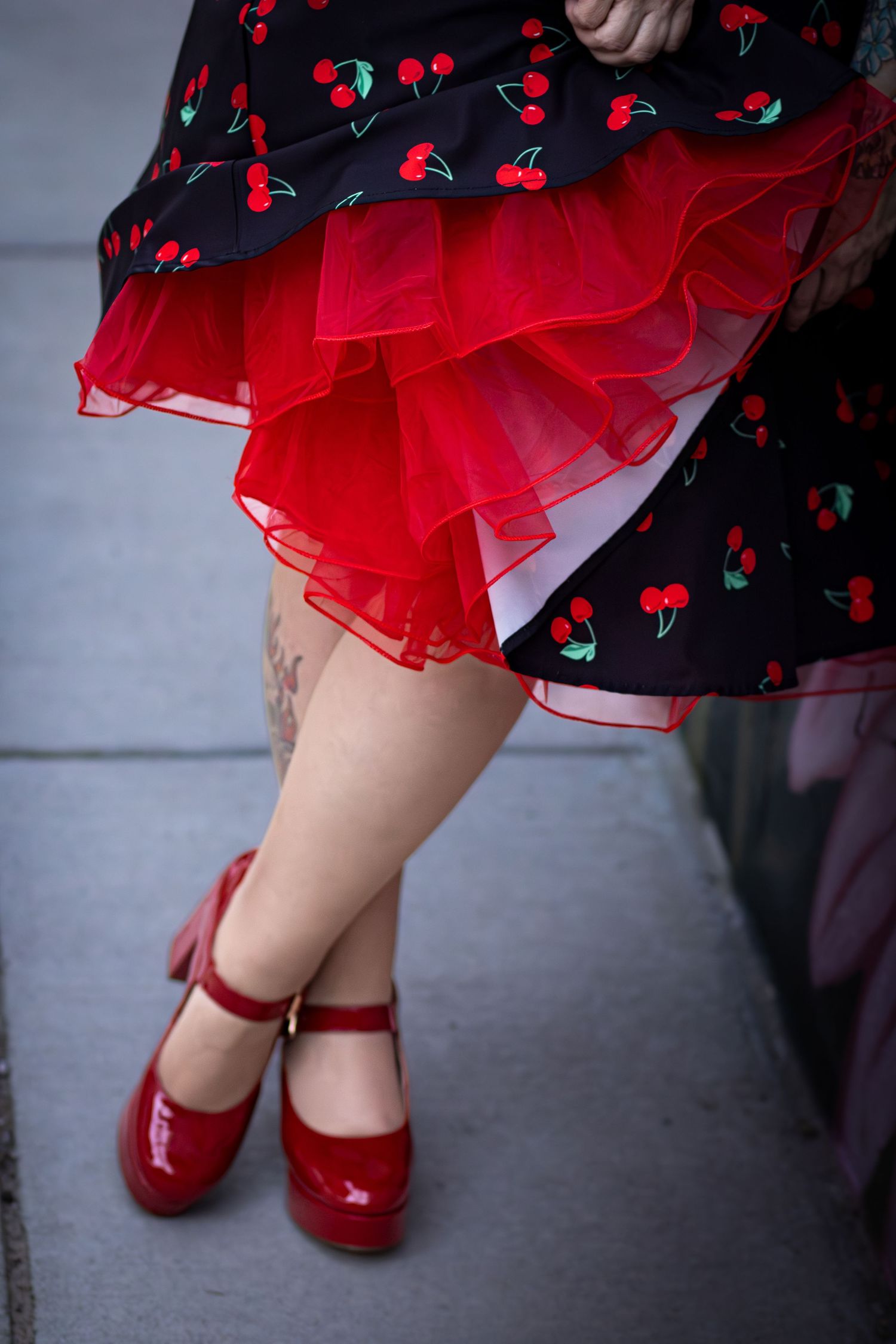 Close-up of cherry print skirt with red tulle petticoat and red patent Mary Jane platform shoes in Monroe, NC.
