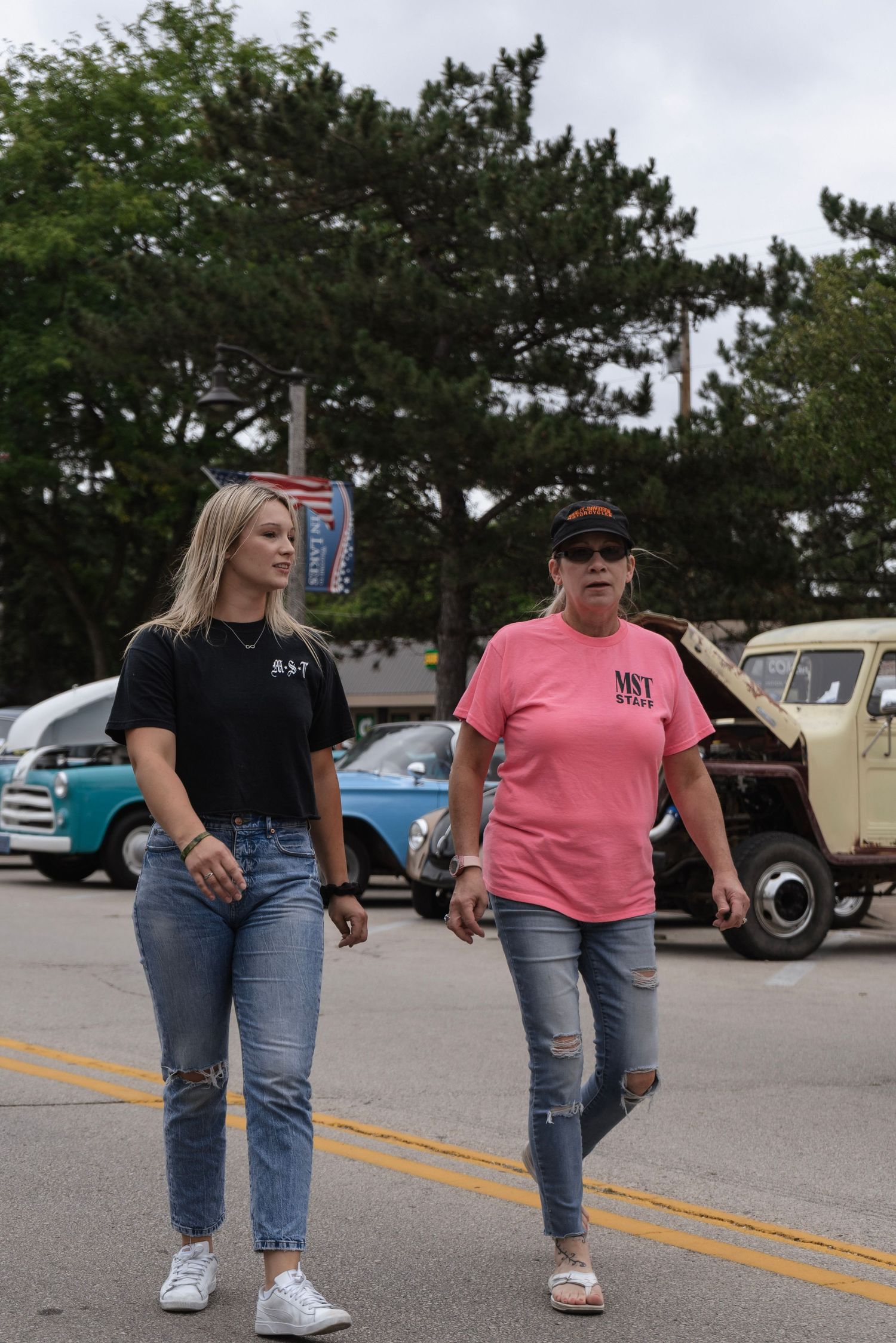 Woman walking at a car show with vintage vehicles visible in the background.