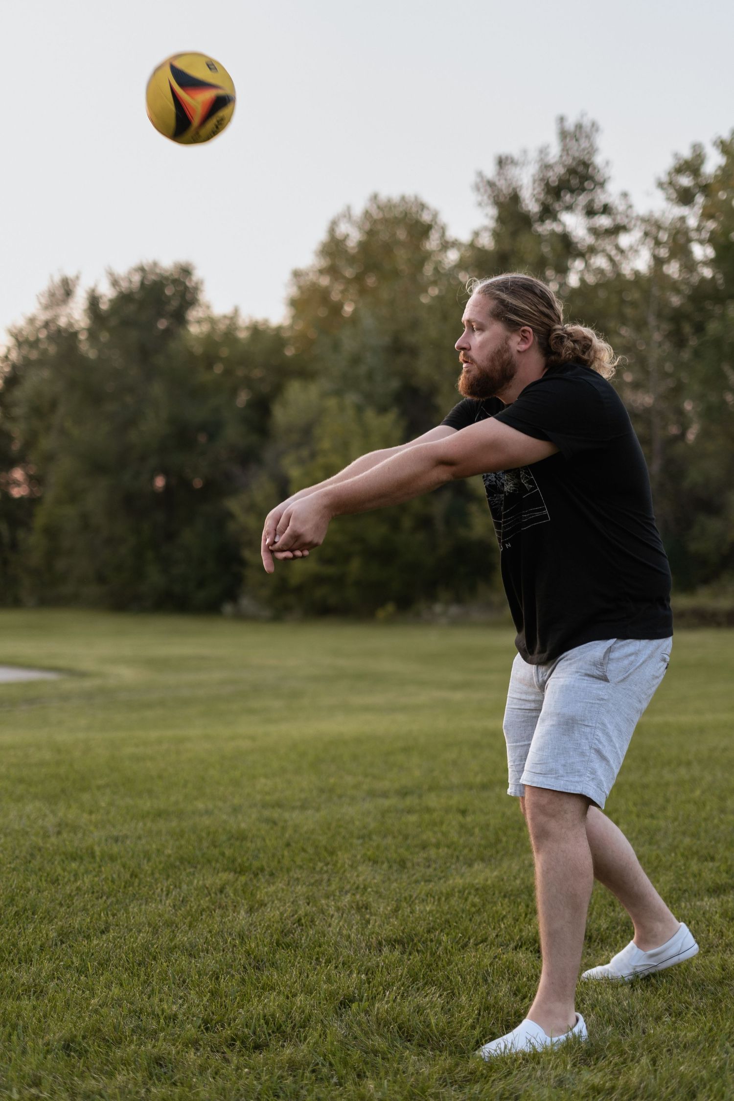 Man playing volleyball on a grassy field during golden hour.
