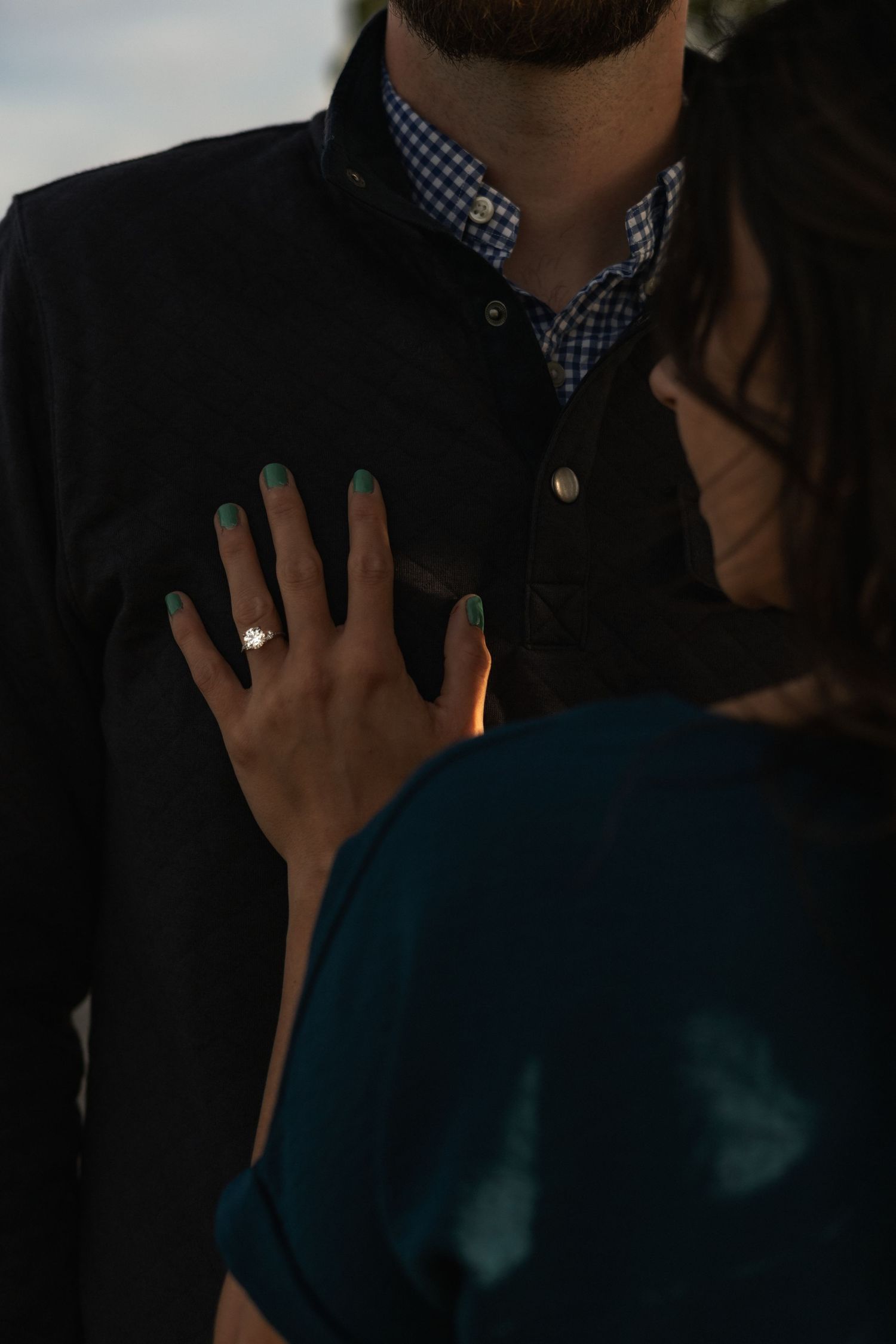 Hand displaying a sapphire engagement ring on dark background with checkered blue and white shirt detail.