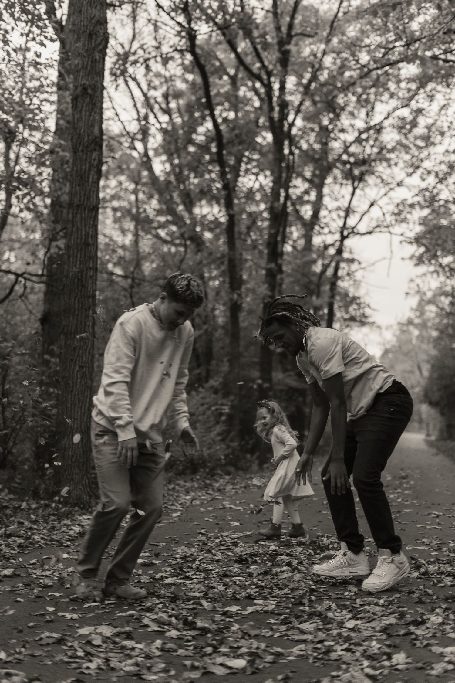 Family playing together on a leaf-covered path in black and white.