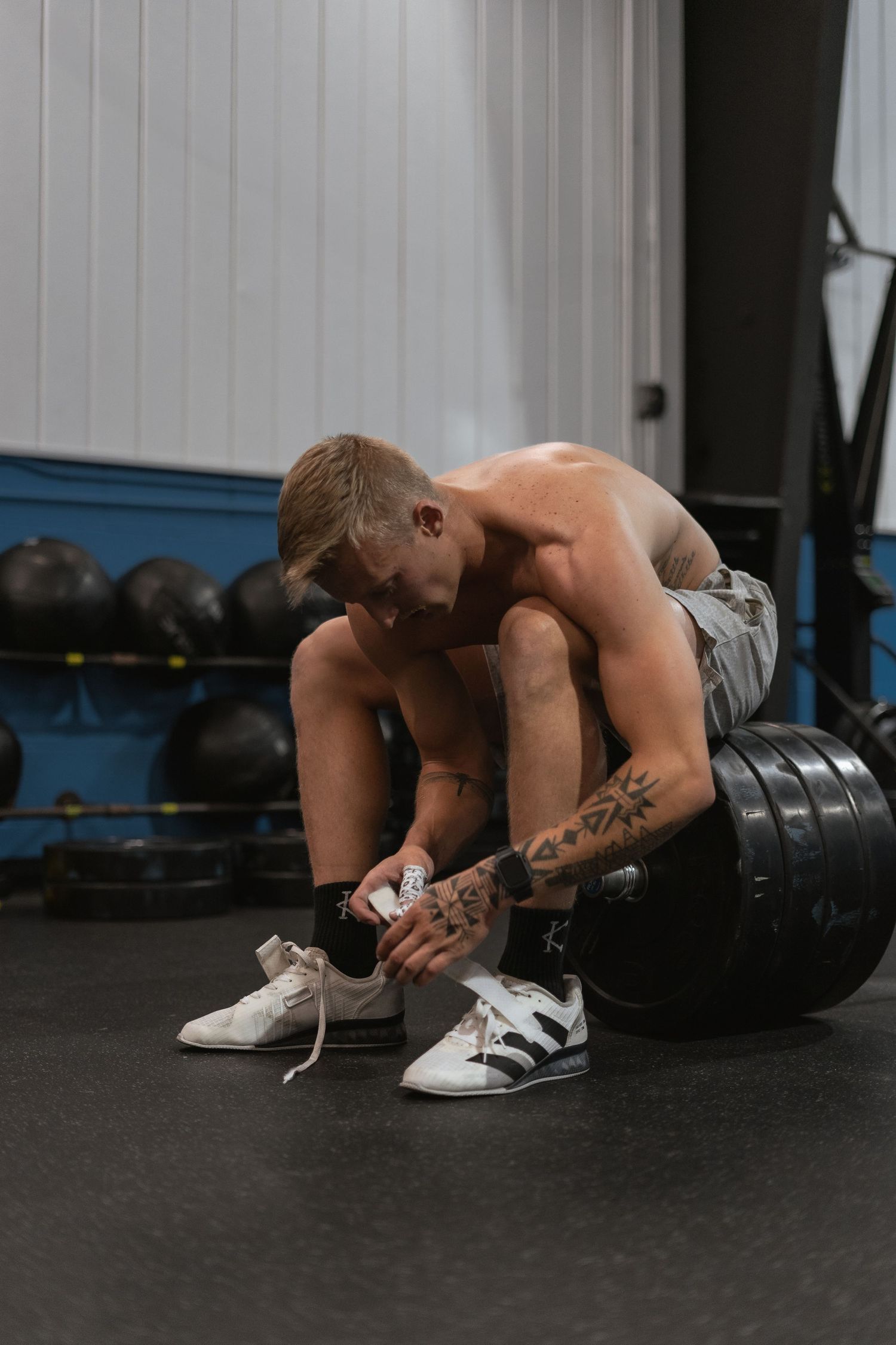 A muscular person tying shoelaces while resting between workouts at the gym.