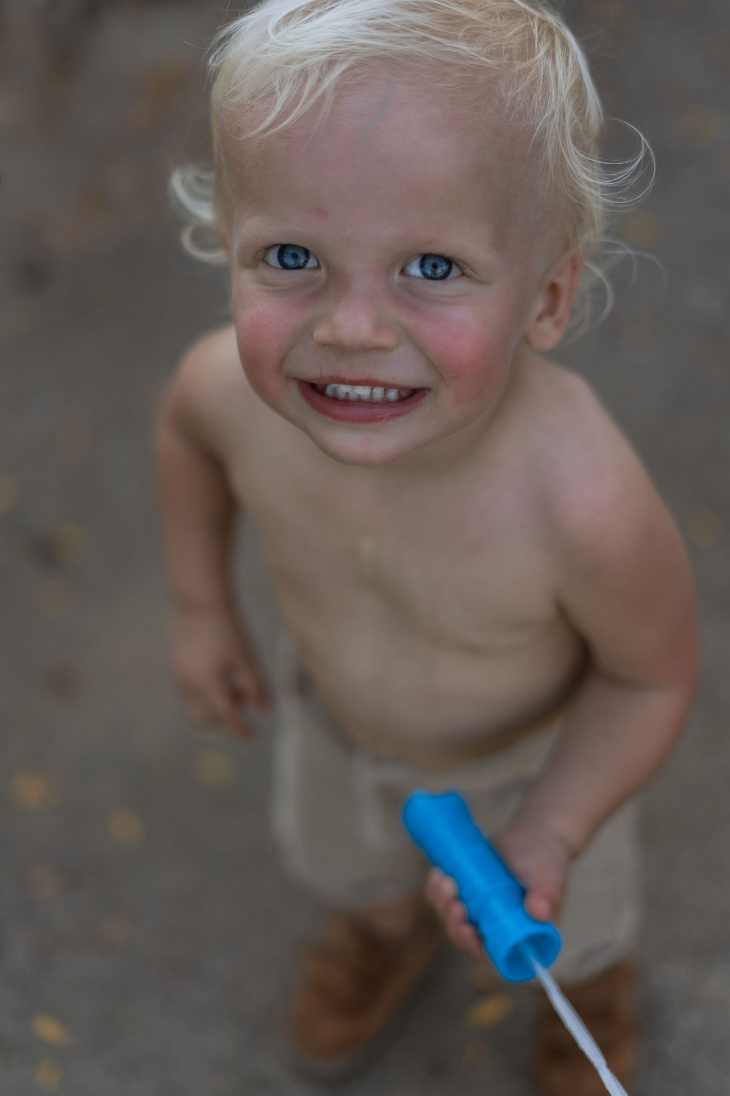 A small child holding a blue toy smiles brightly at the camera.