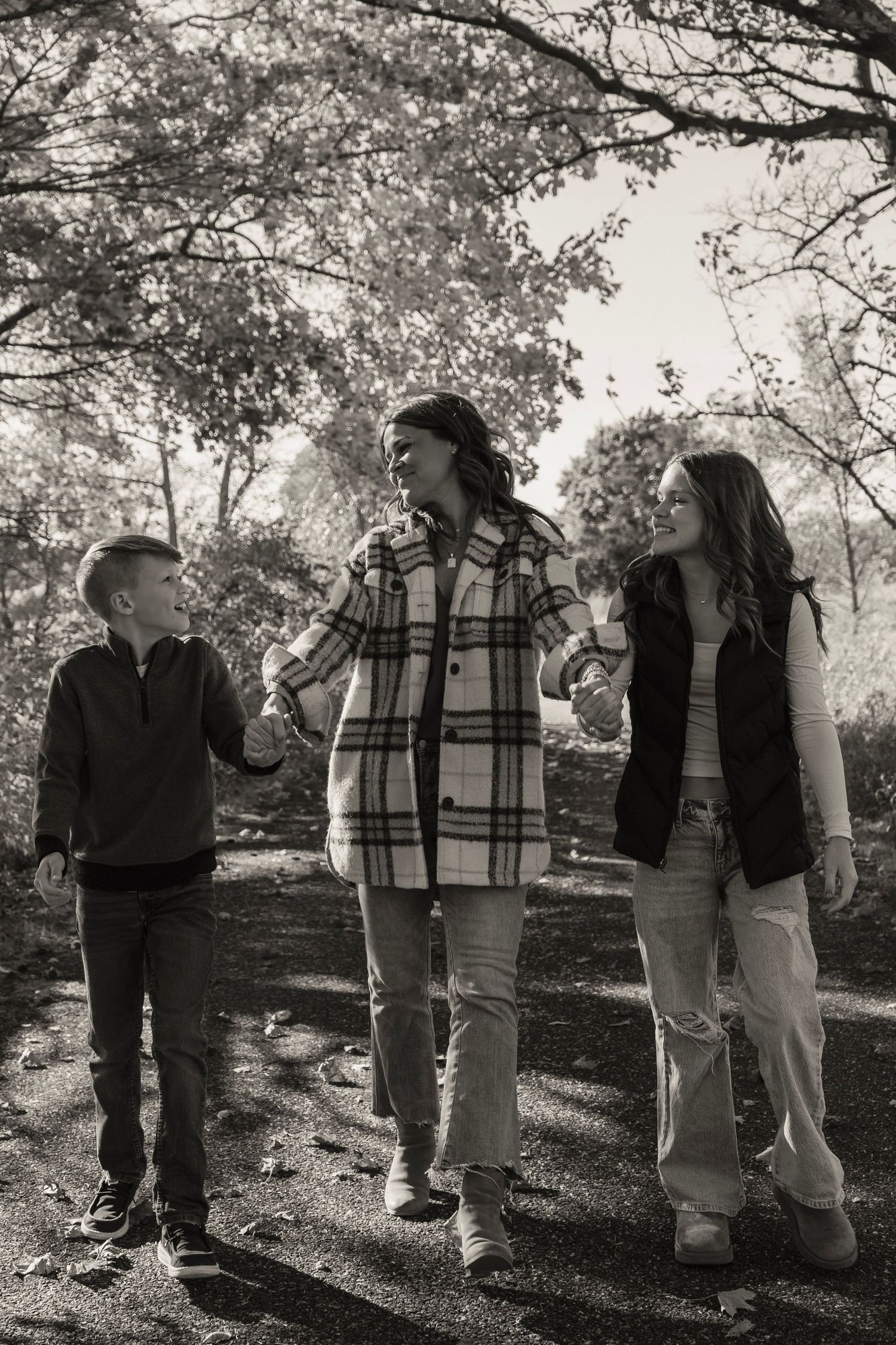 Family walking and talking together on a wooded path in casual fall attire.