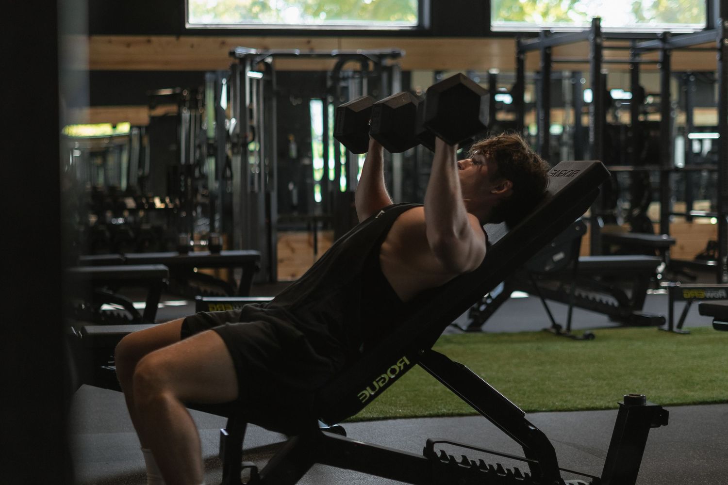 Athlete exercising with dumbbells on an incline bench in a dimly lit gym setting.