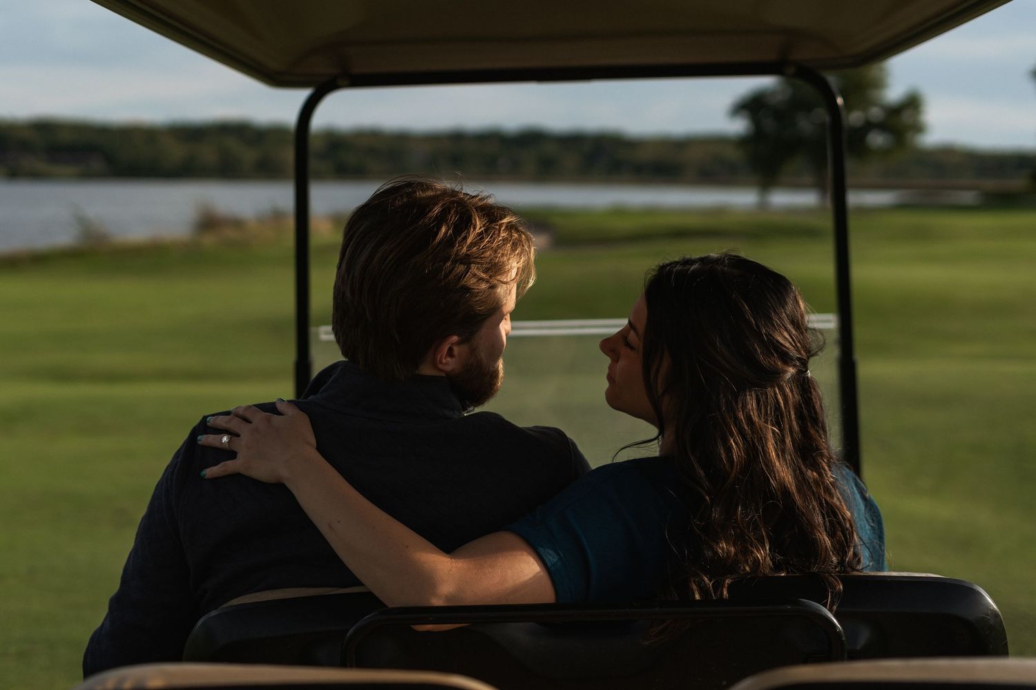 Two people sitting in a golf cart on a sunny day at a golf course.
