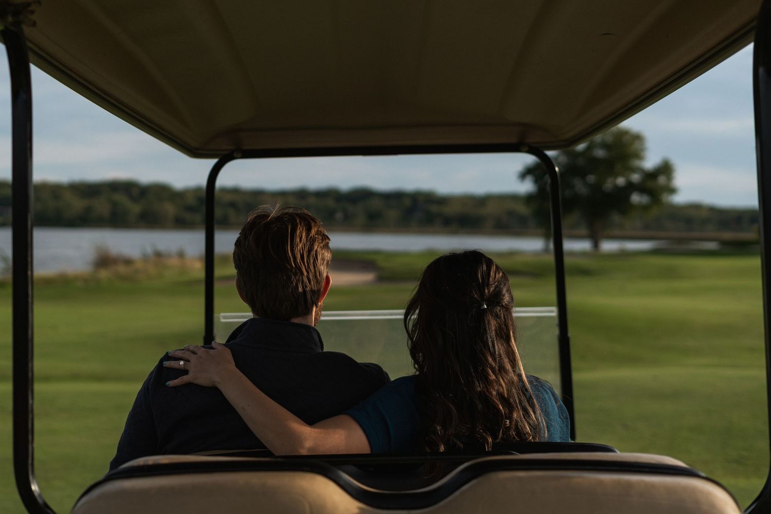 Couple riding in golf cart overlooking scenic lake and golf course on sunny day.
