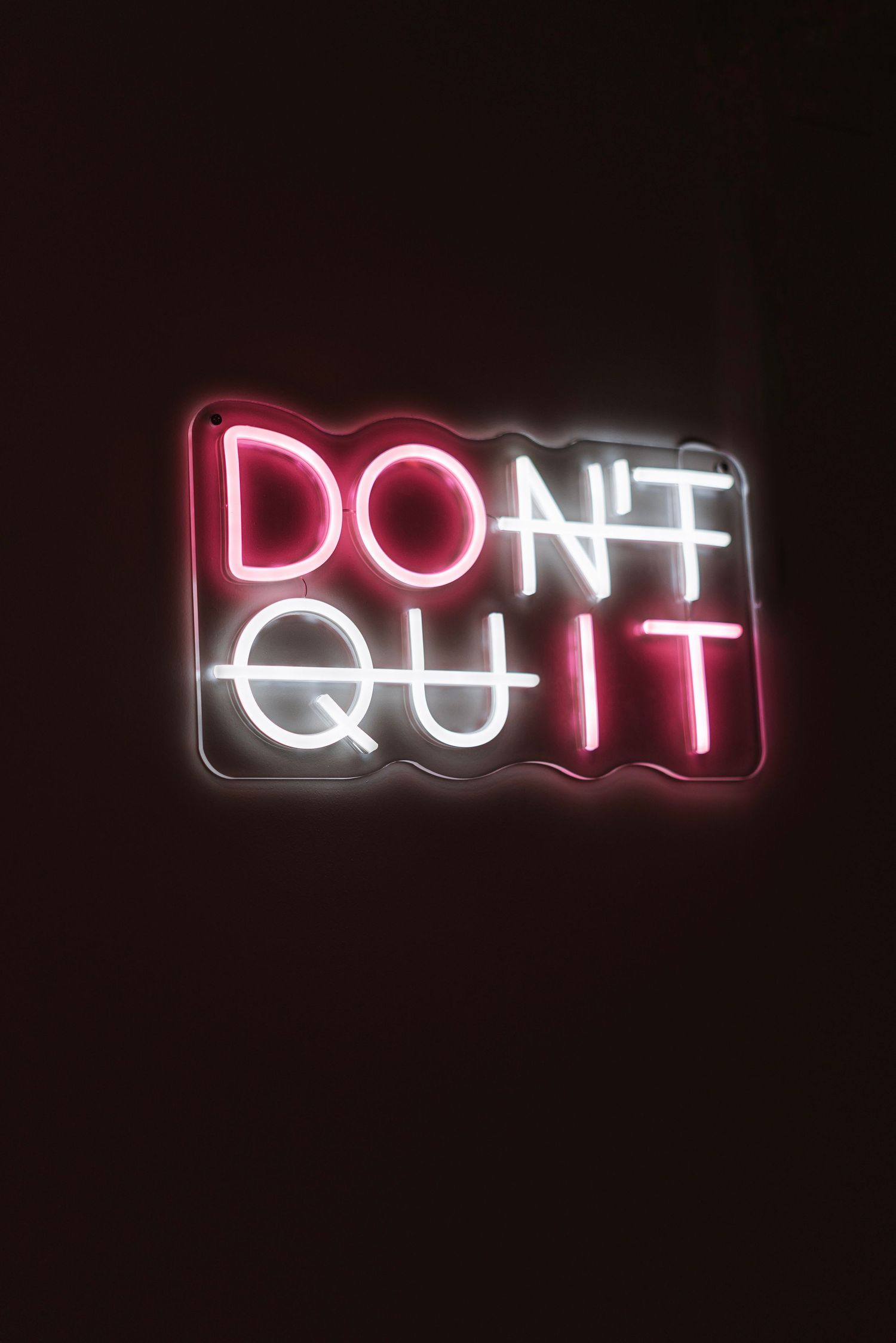A neon sign displaying 'DON'T QUIT' glows in red and white against a dark background.