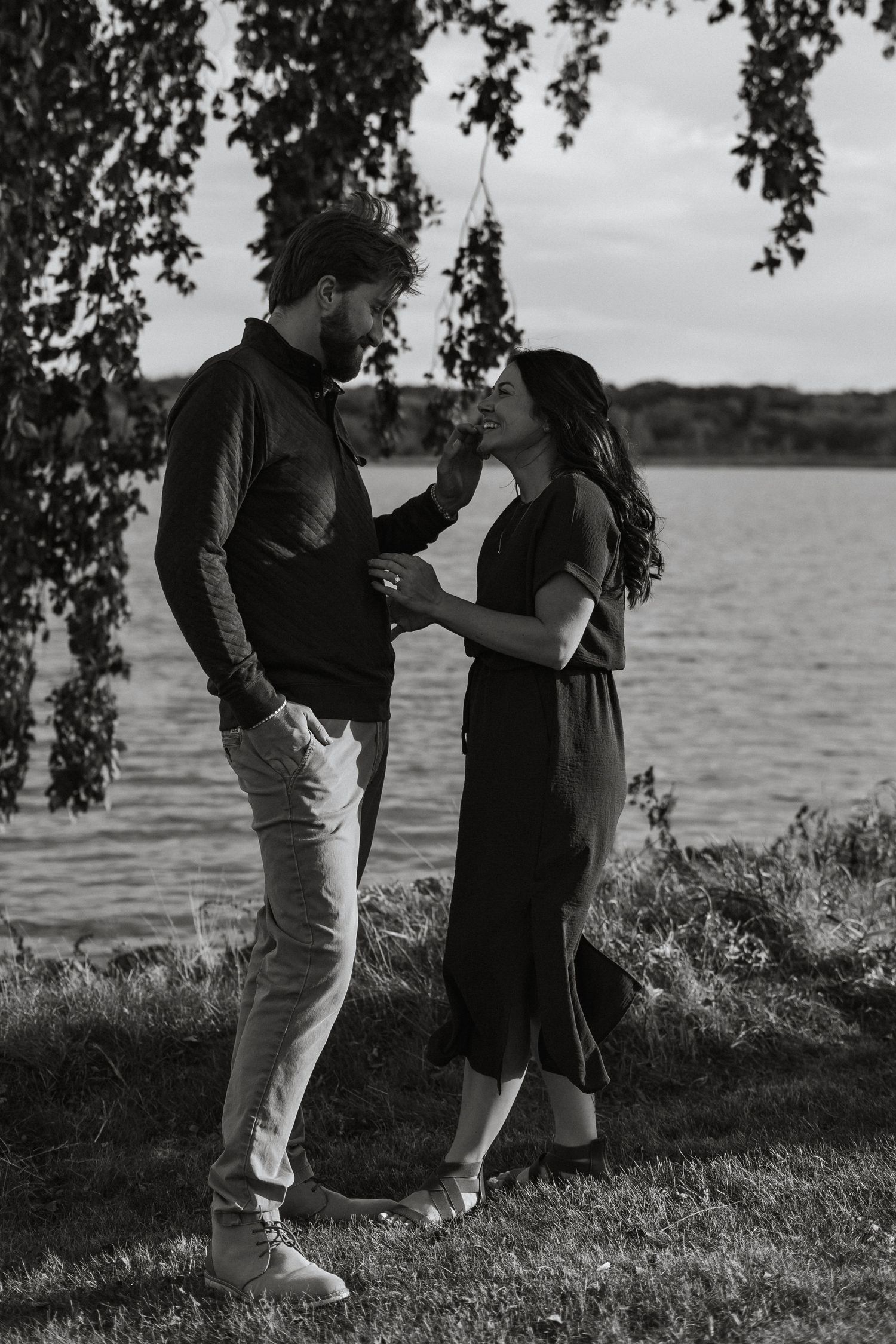 A couple stands together near a lake shore under a hanging tree in a series of black and white vintage-style photos.