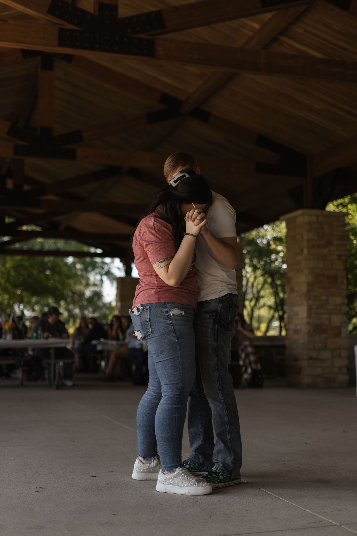 Couple embracing under covered outdoor structure in casual attire.