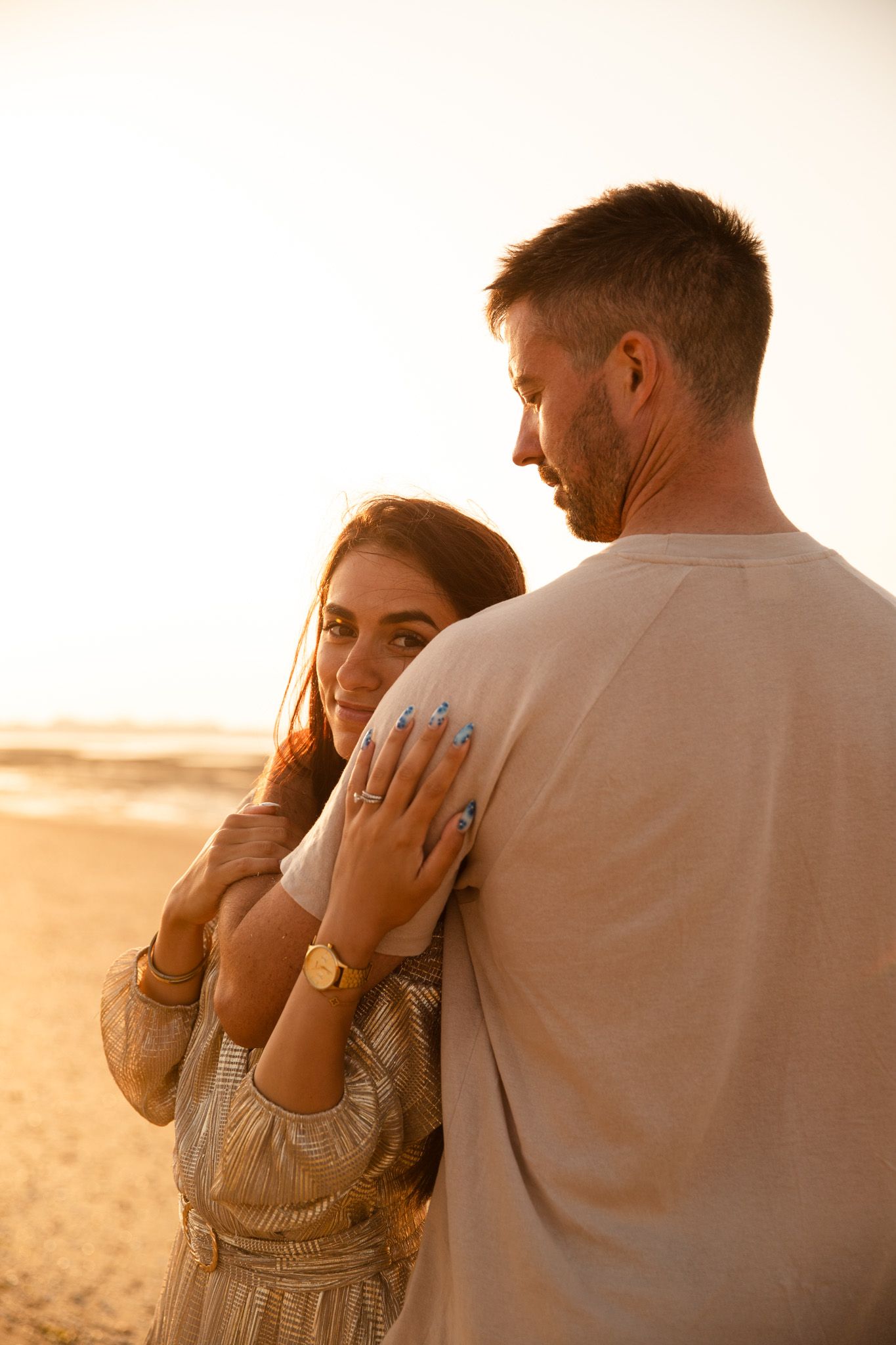 A couple embraces on a sunlit beach at golden hour, creating a romantic silhouette against the warm sky.