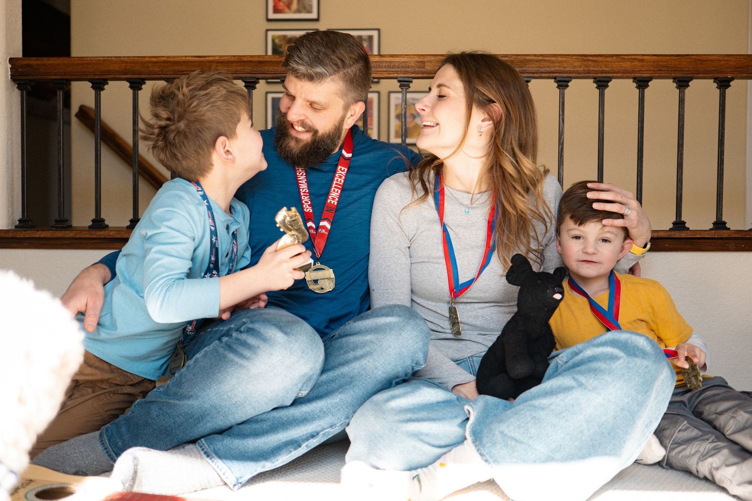 Family of four sitting against stair railing, all wearing medals in celebration of recent Olympics during family photo session.